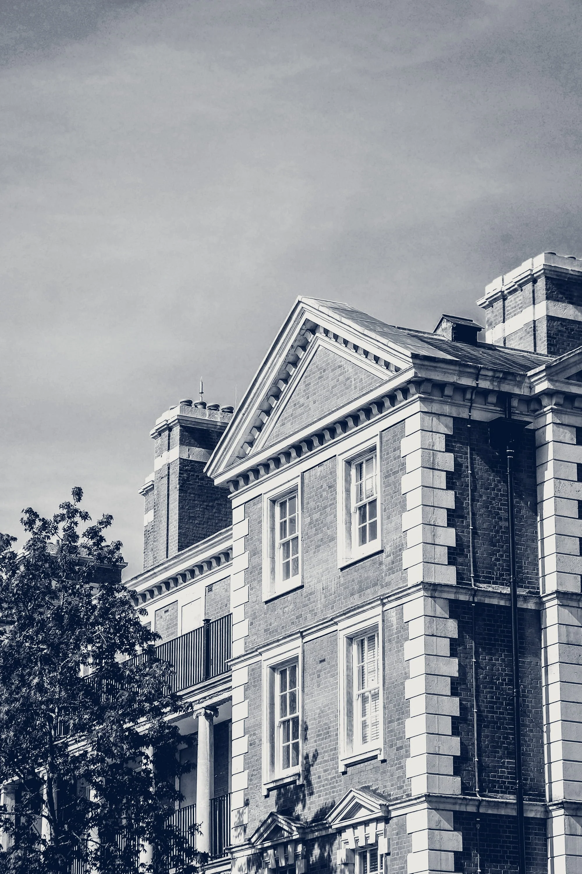 A black and white photo of a historic brick building with decorative white accents, tall windows, and chimneys on the roof.