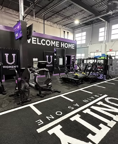 Gym equipment at a sports facility with a 'WELCOME HOME' sign and a marked running lane on the floor.