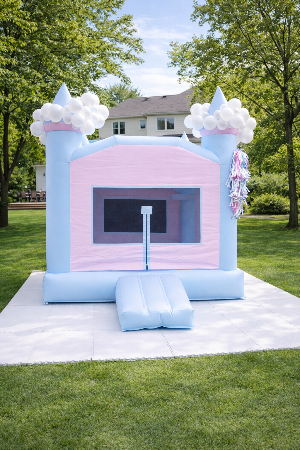 Inflatable pink and blue castle bounce house with white clouds and turrets, set up on a grassy yard during daytime.