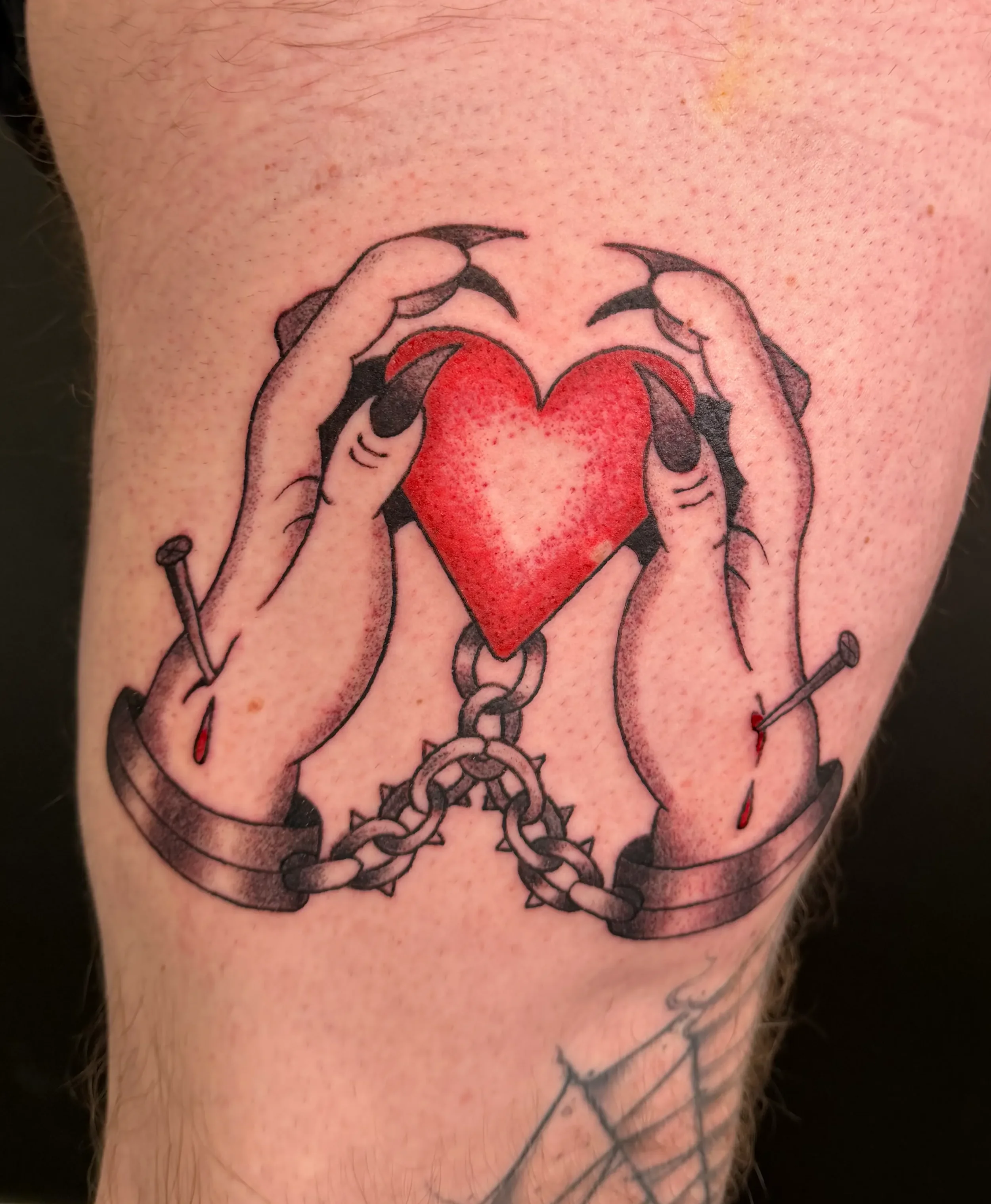Tattoo mit Händen, die ein rotes Herz halten, verbunden mit Ketten und einem Schlüssel. Die Hände sind gefesselt, die Ketten sind geöffnet.
