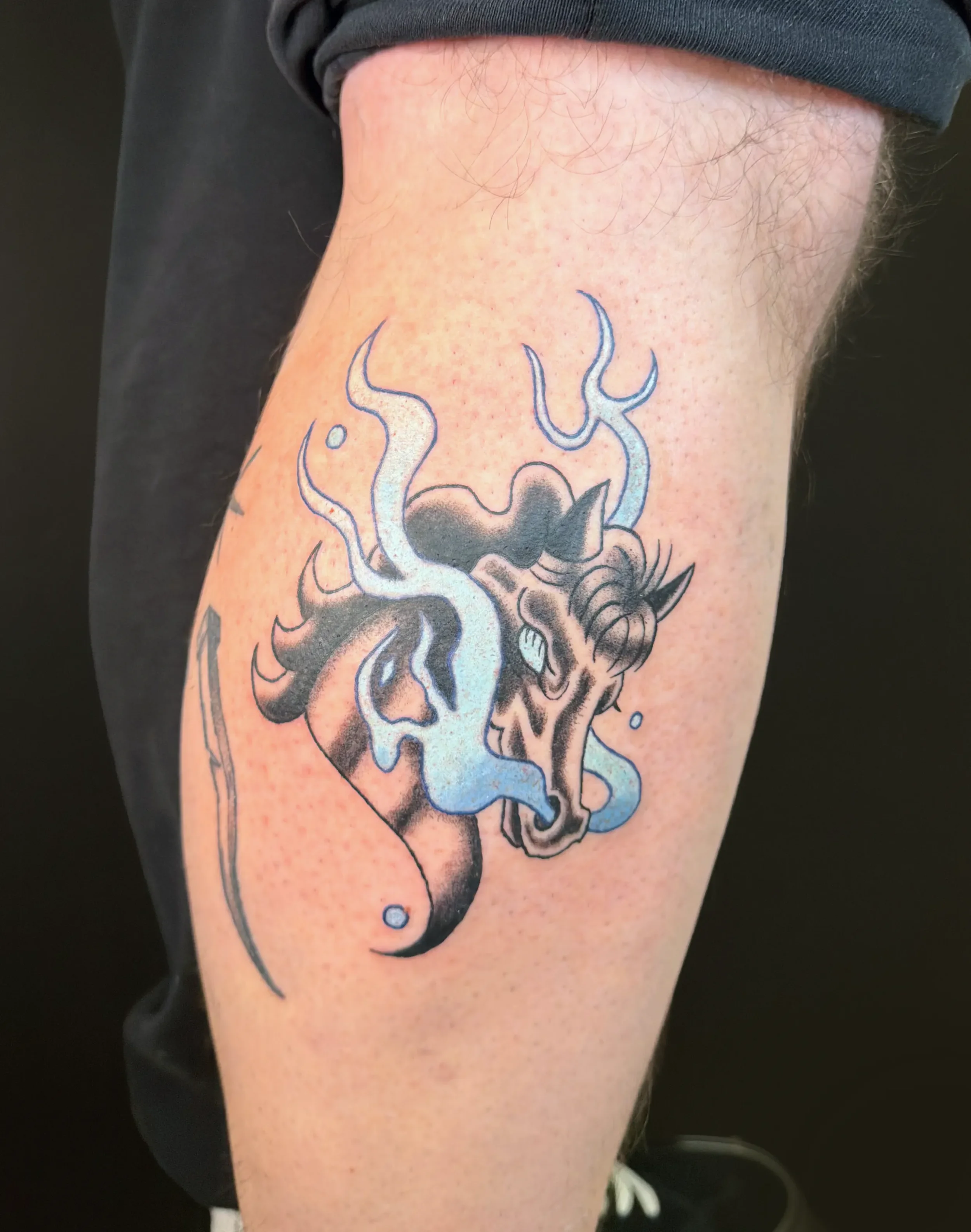 Tattoo eines kopfbewussten, kämpferischen Wolfsgesichtes mit bläulichen Rauchspiralen auf dem Oberarm.