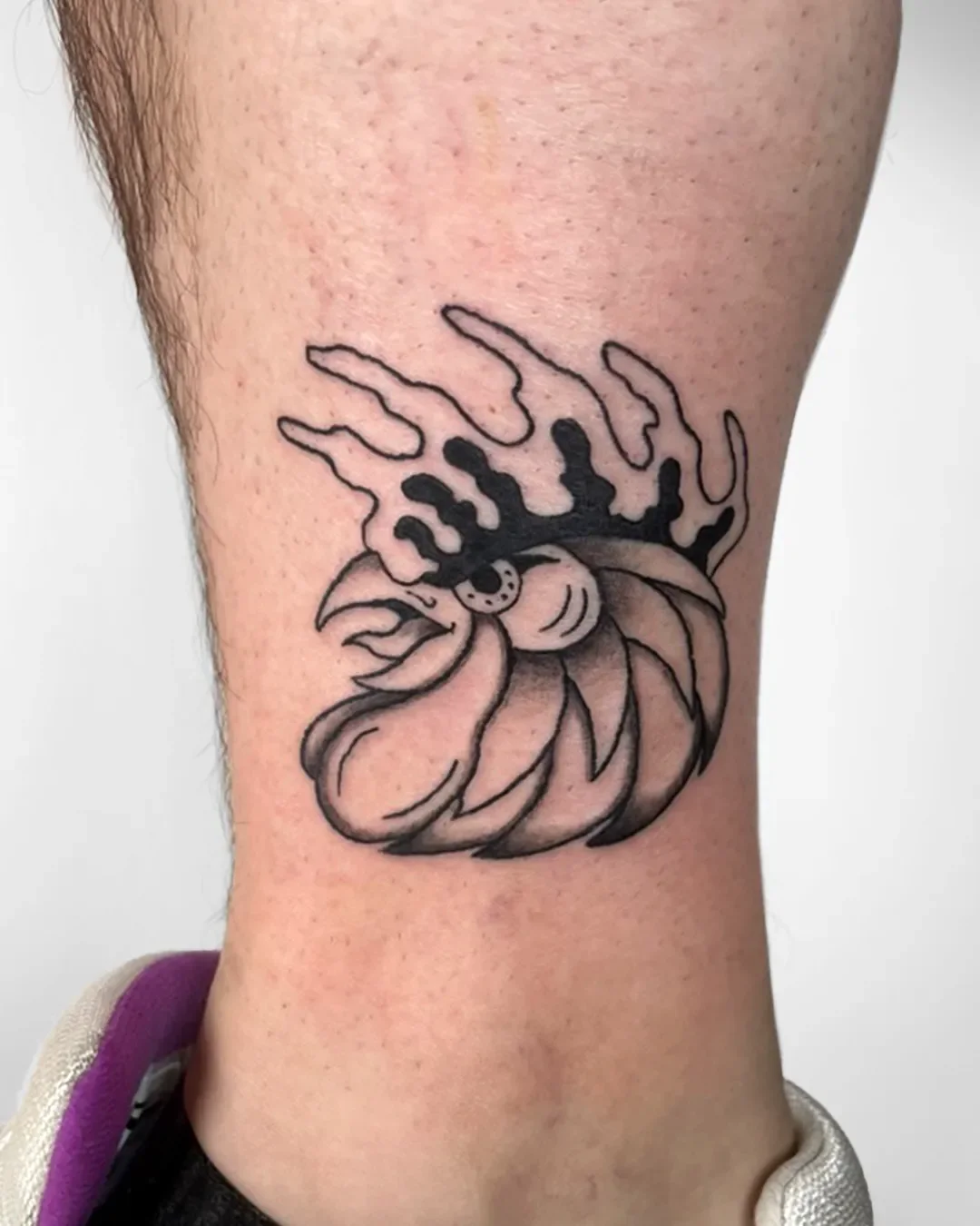 Tattoo eines stylisierten Schmetterlings auf der Wade, mit dunklen Linien und Schattierungen, in Schwarz gehalten.