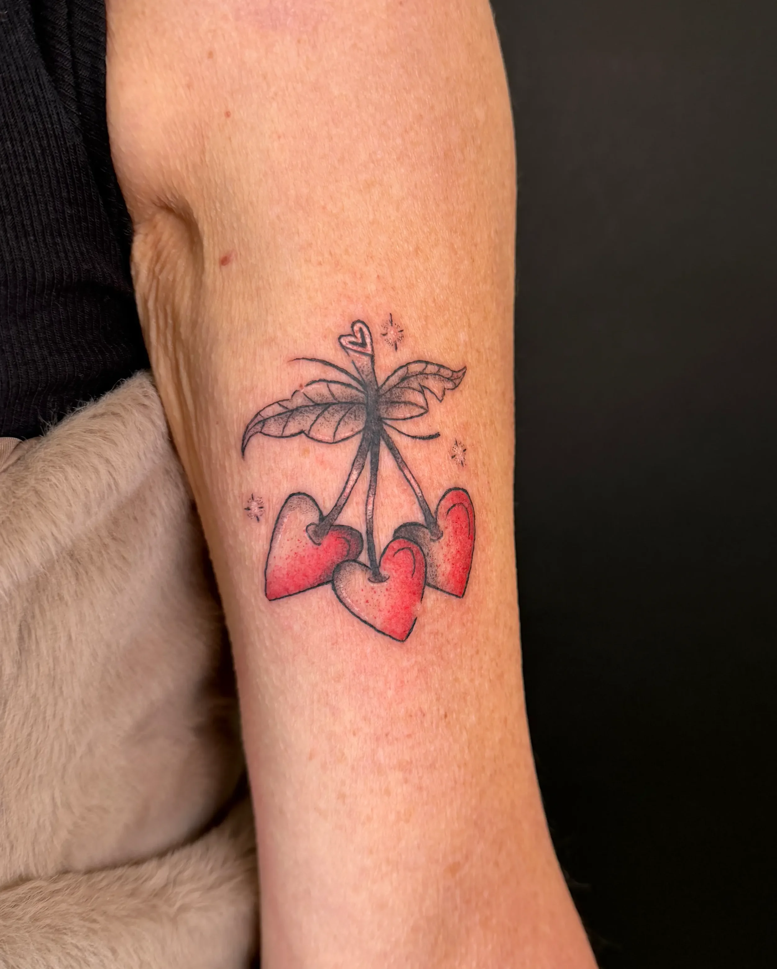 Eine Tätowierung auf dem Oberarm zeigt einen Schmetterling, dessen Flügel aus roten Herzen bestehen, und einige kleine Sterne um ihn herum.