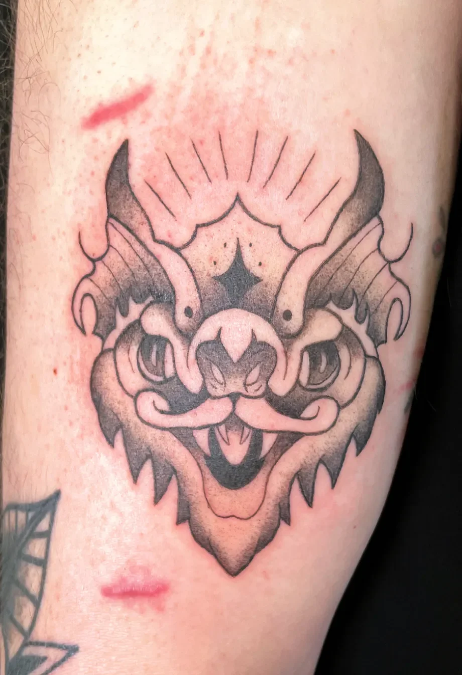 Schwarze Tätowierung eines Drachenkopfs auf menschlicher Haut.