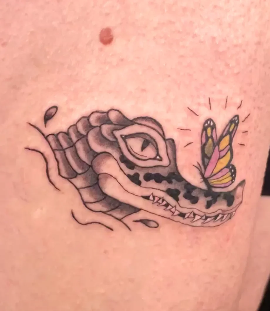 Tattoo eines Krokodils mit einer bunten Schmetterlingsflügel auf dem Kopf.