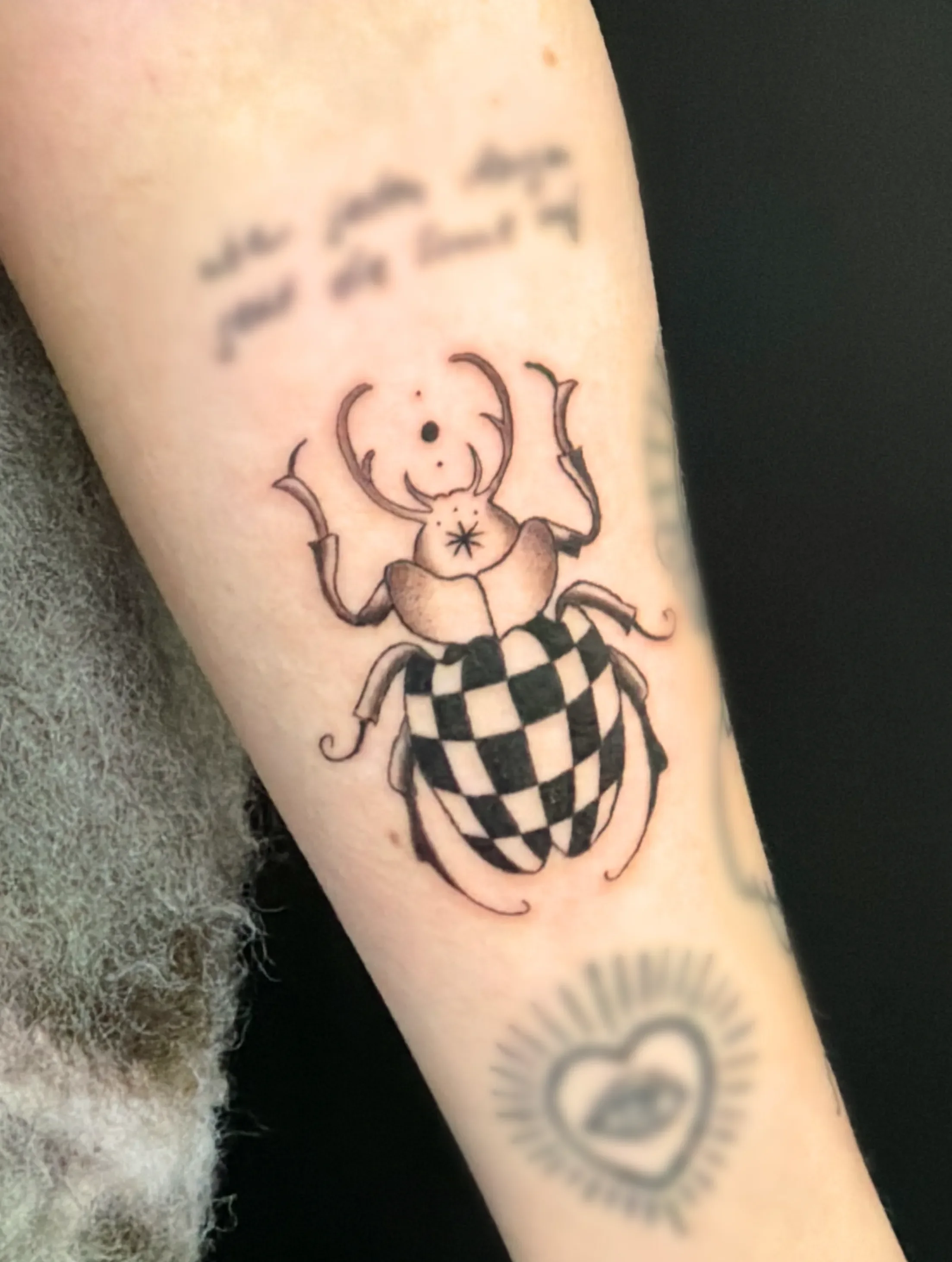 Tattoo eines Käfers mit einer schwarz-weißen karierten Muster auf dem Rücken, auf dem Unterarm.