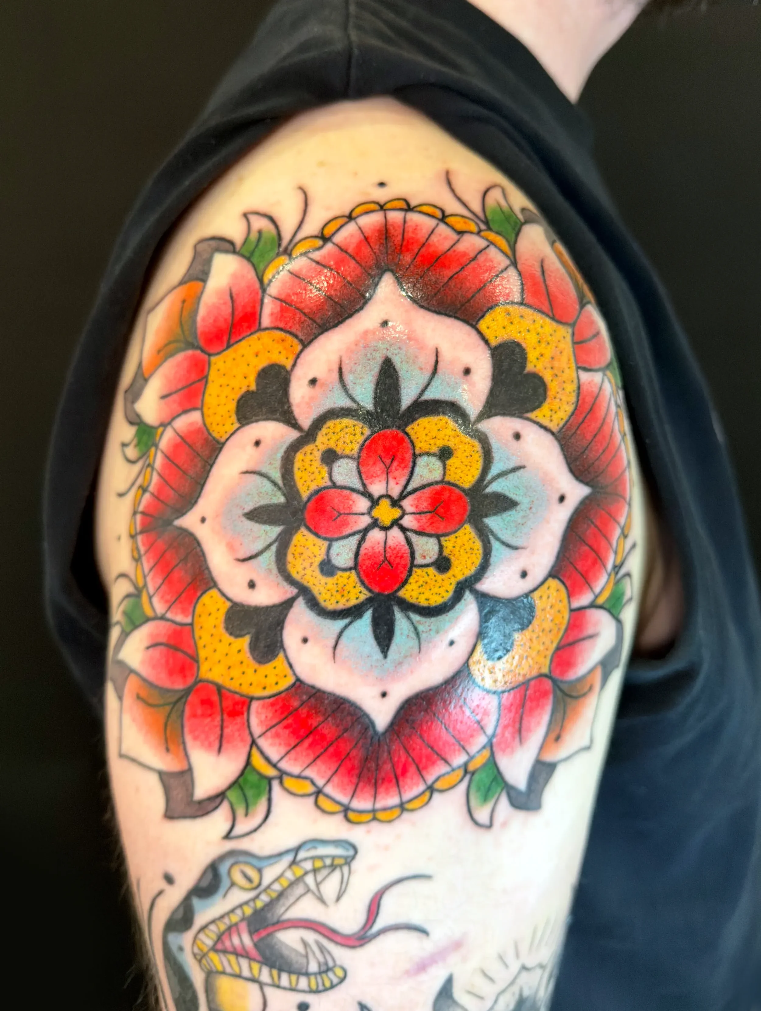 Farbenfrohe traditionelle japanische Tätowierung eines Blumenmusters auf dem Oberarm mit einer Schlange darunter.