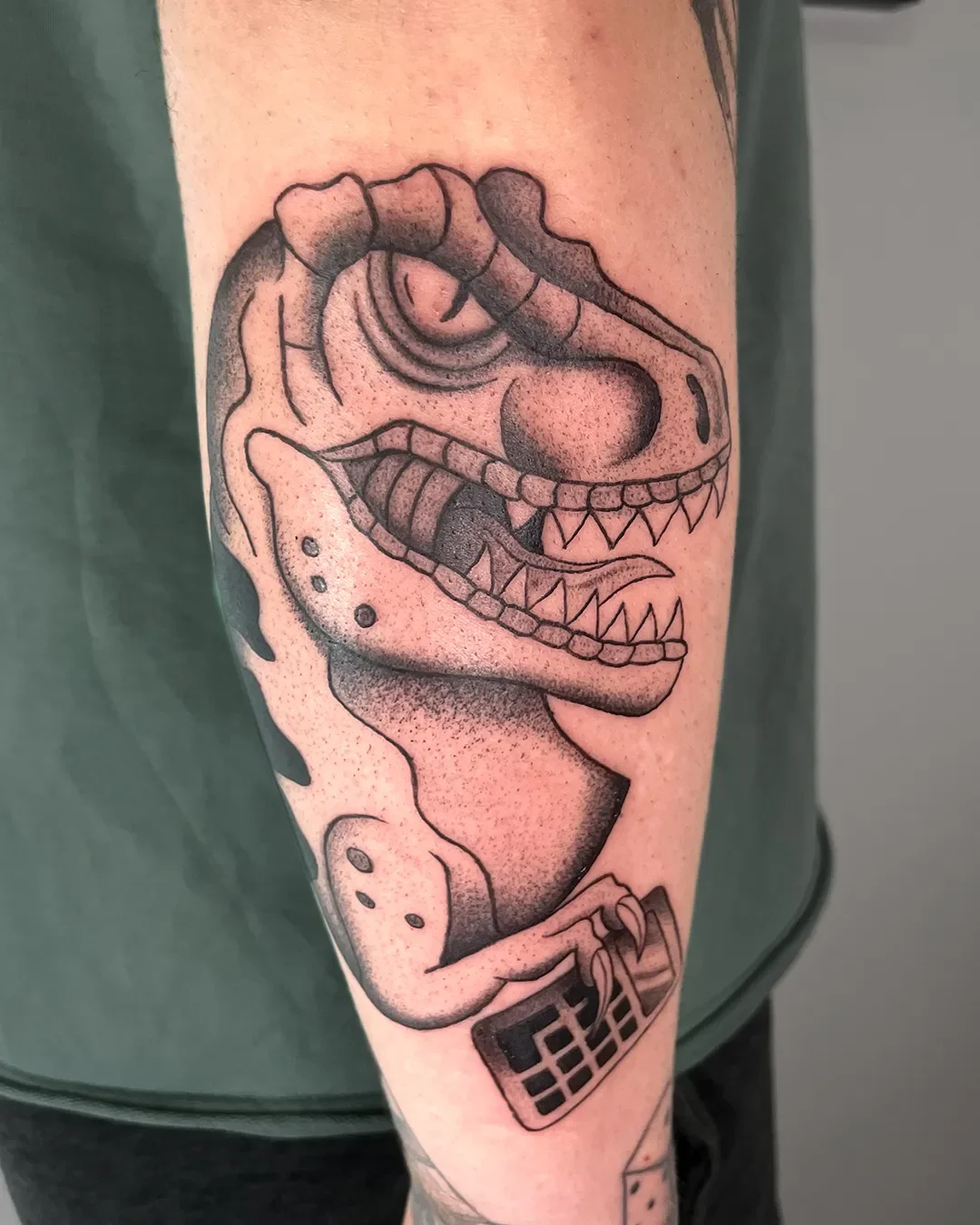 Tattoo eines Dinosauriers auf dem Oberarm, gezeichnet im Stil eines traditionellen Fantasy-Designs.