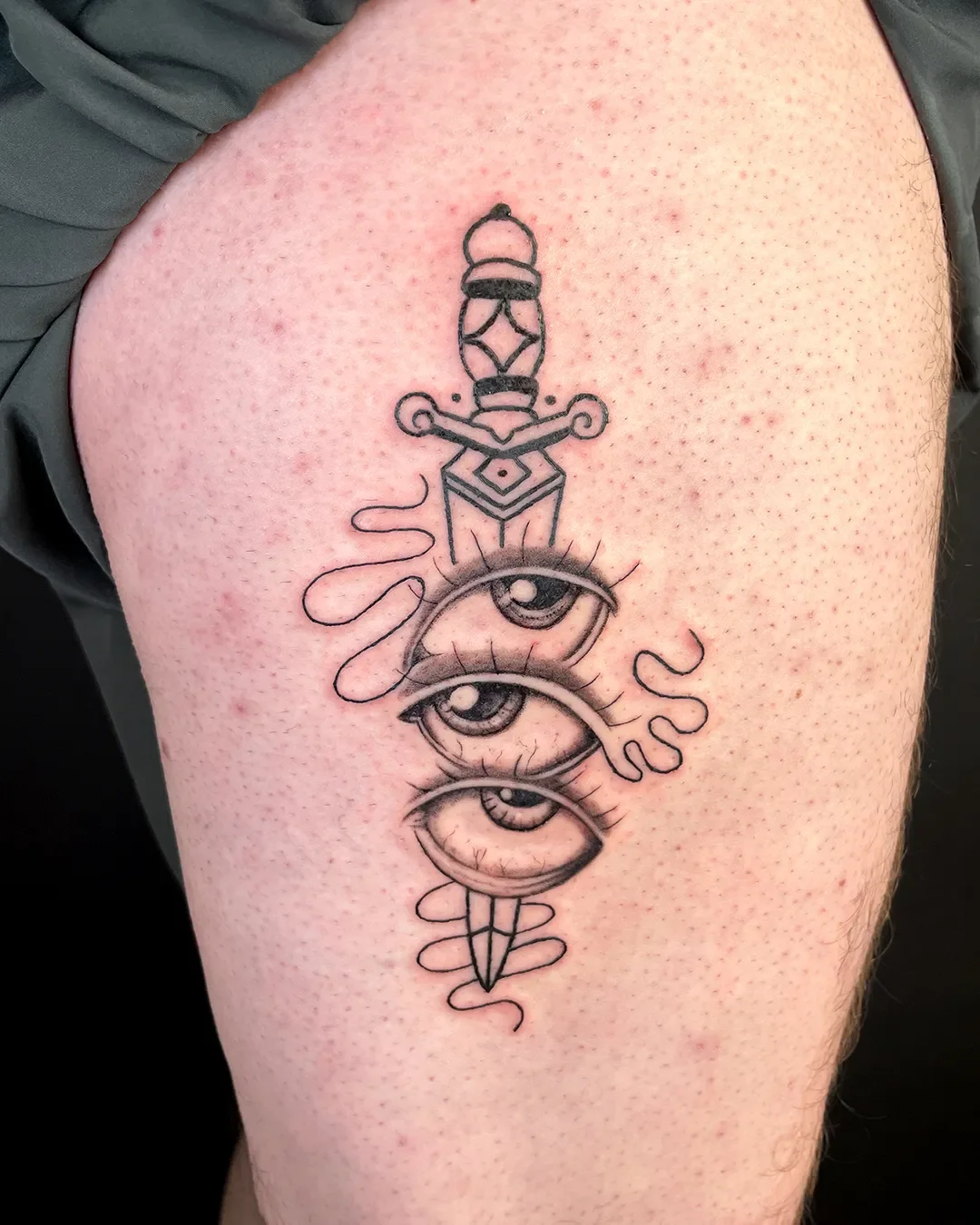 Tattoo auf der Oberschenkel mit drei Augen, einem Dolch, einer Lampe und abstrakten Linien.