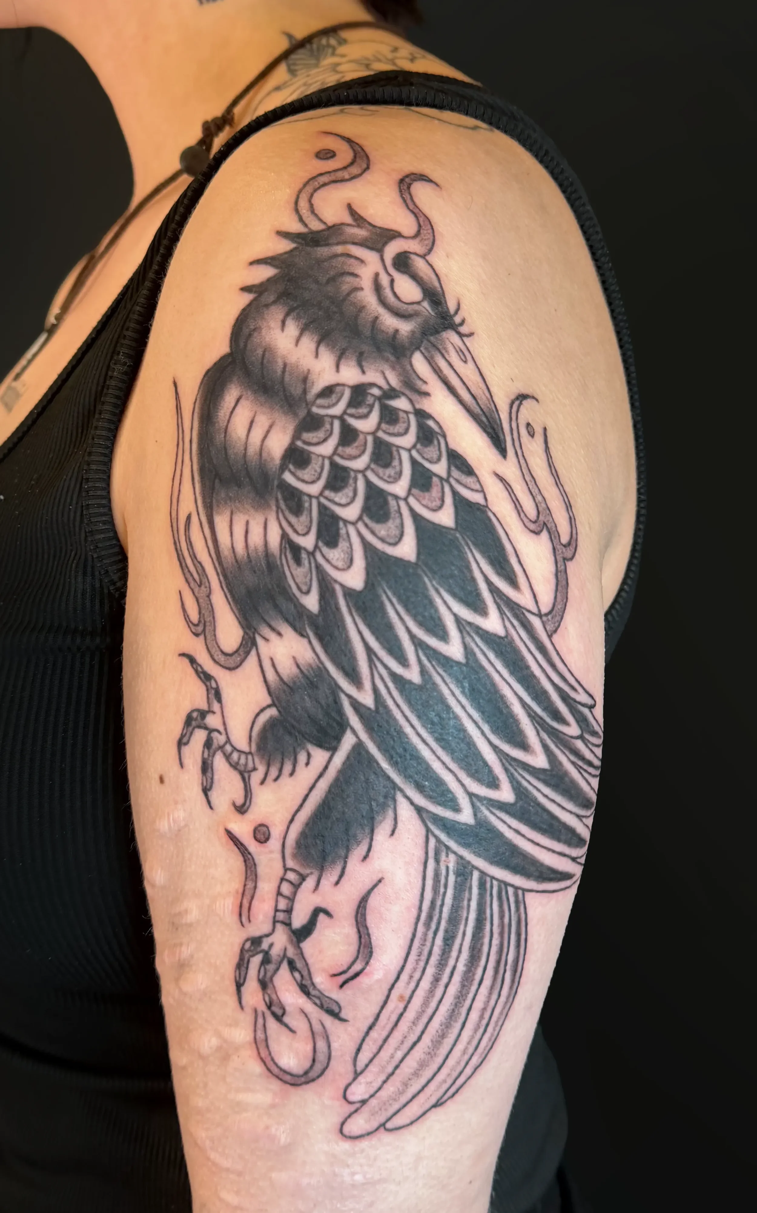 Schwarze Tätowierung eines stilisierten Vogels, vermutlich eines Falken oder Adlers, auf einem Oberarm, mit detaillierten Federn und Krallen.