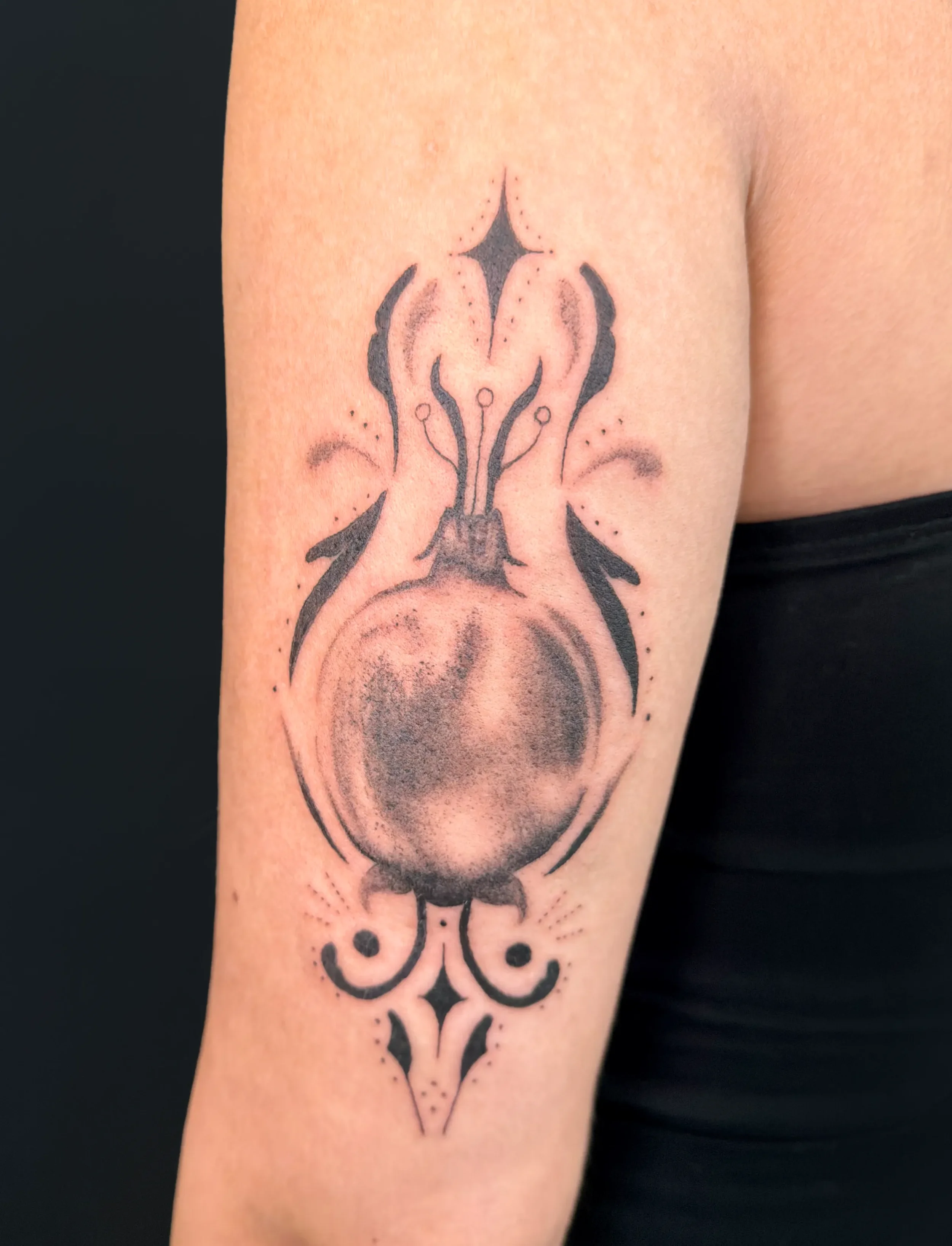 Schwarzes und graues Tattoo einer stilisierten Flasche auf dem Oberarm einer Person.