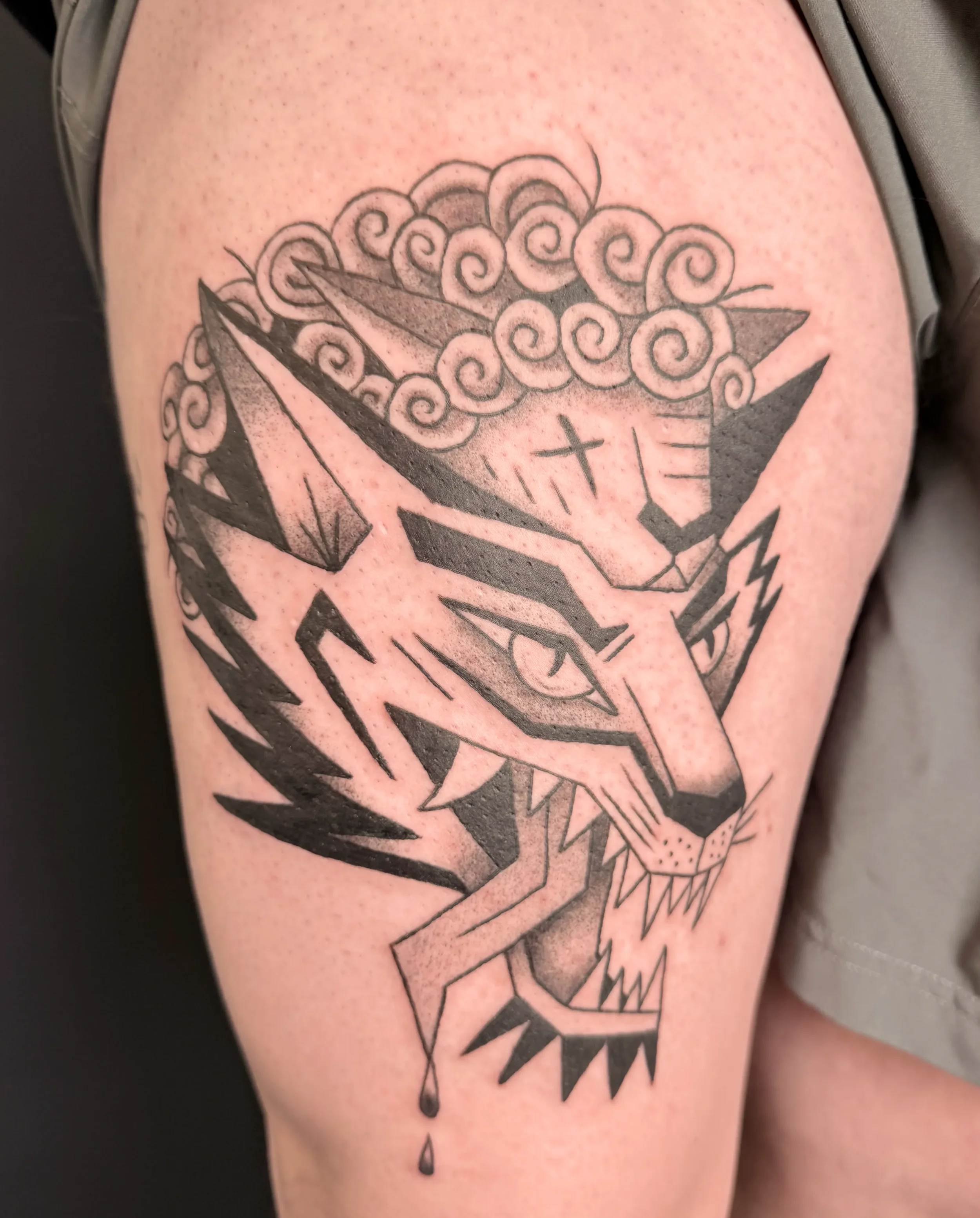 Tattoo eines geometrischen Wolf-Kopfes mit stilisiertem Feuer und einer Karte. Einige Symbole sind sichtbar, darunter ein Kreuz und ein Tropfen.
