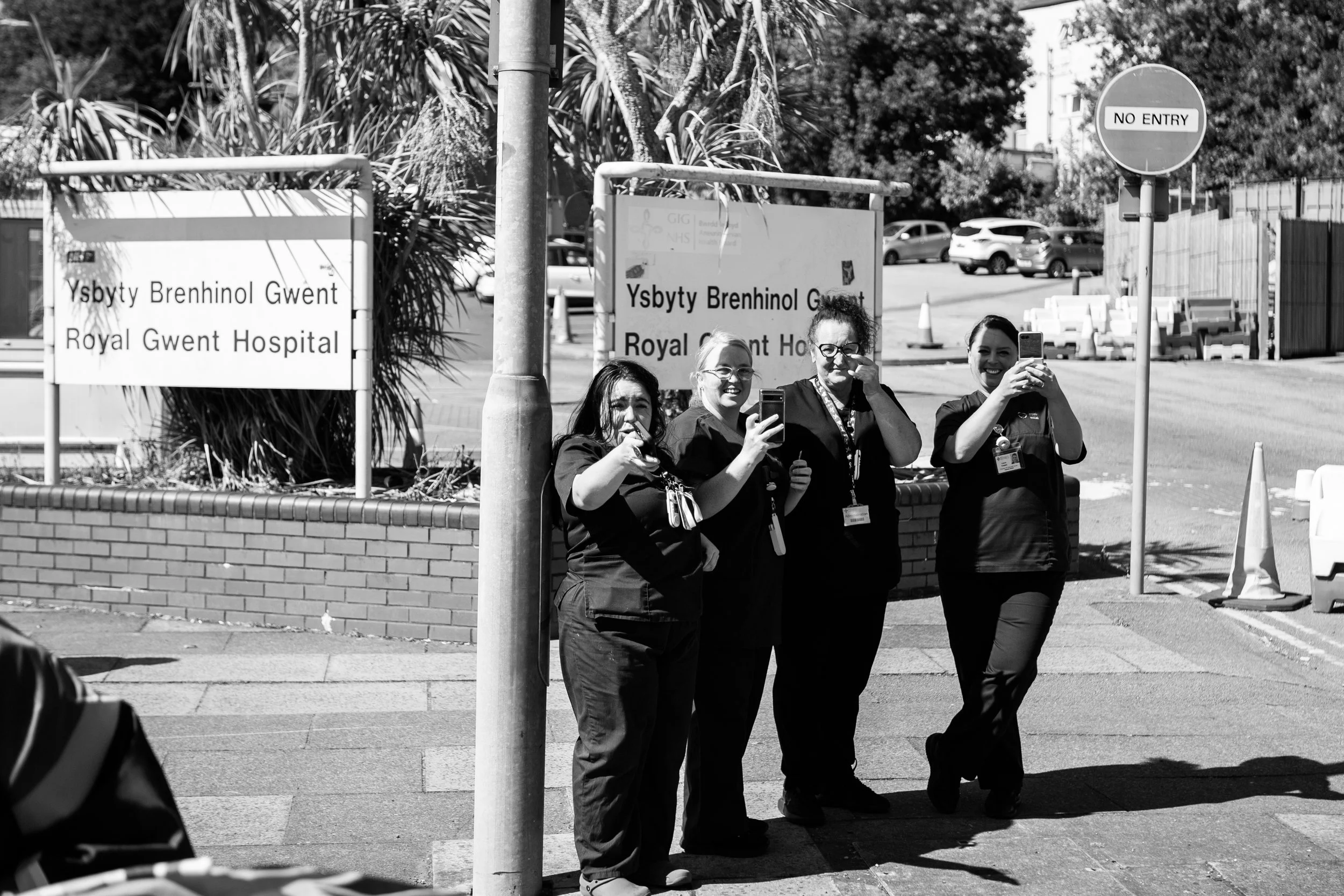 Four women nurses standing outside Royal Gwent Hospital, taking photos with their phones.
