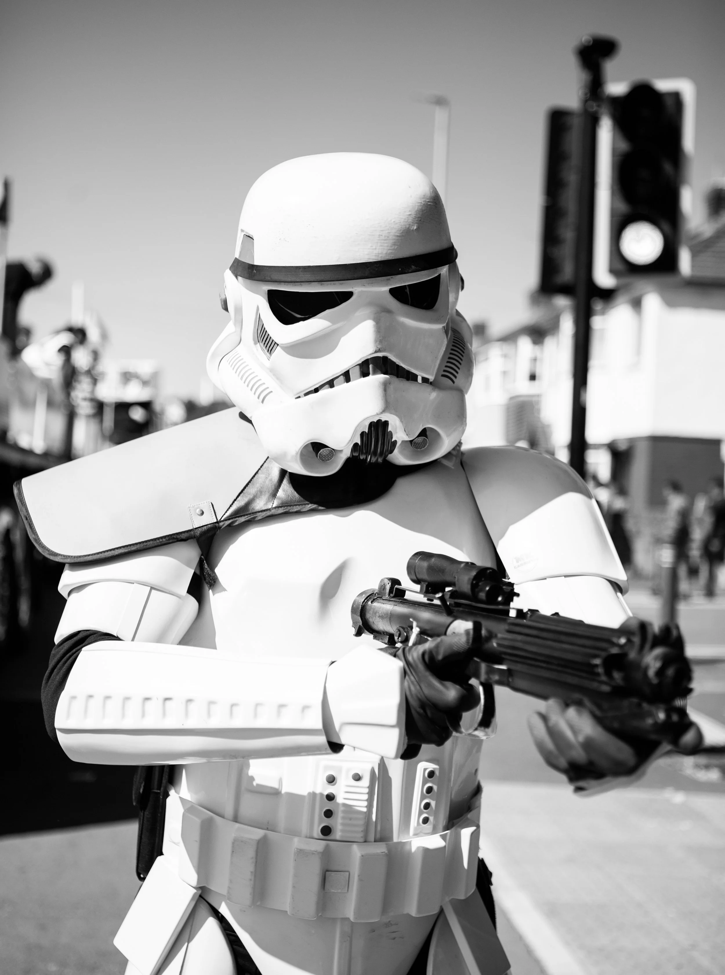 A person dressed as a stormtrooper from Star Wars holding a gun in an urban setting with traffic lights in the background.