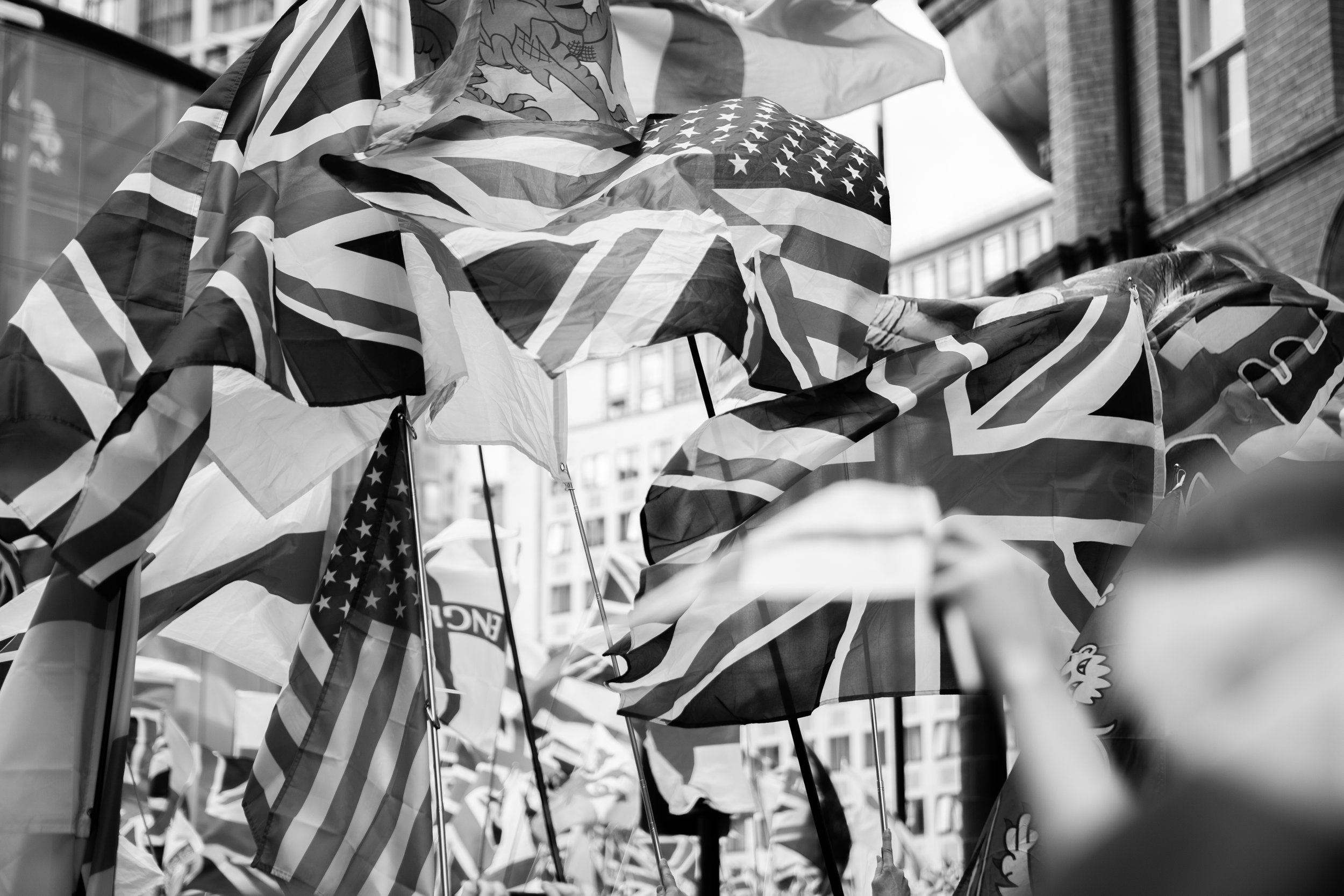 Black and white photo of multiple flags, including the United States and United Kingdom flags, on a city street.