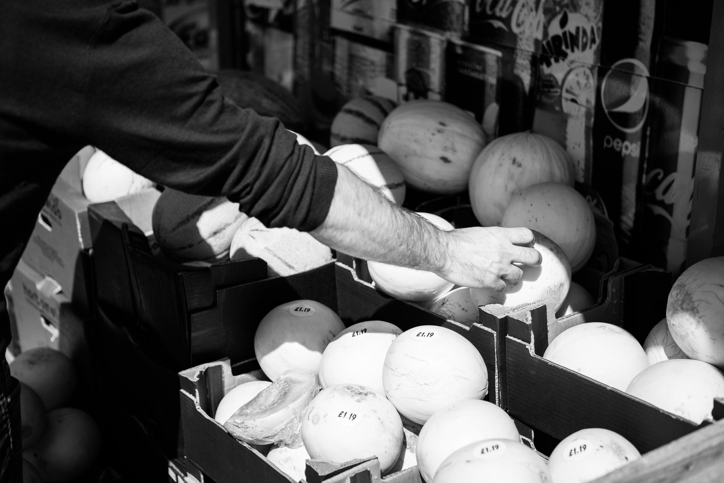 A person reaching for a melon on display at a market or grocery store.