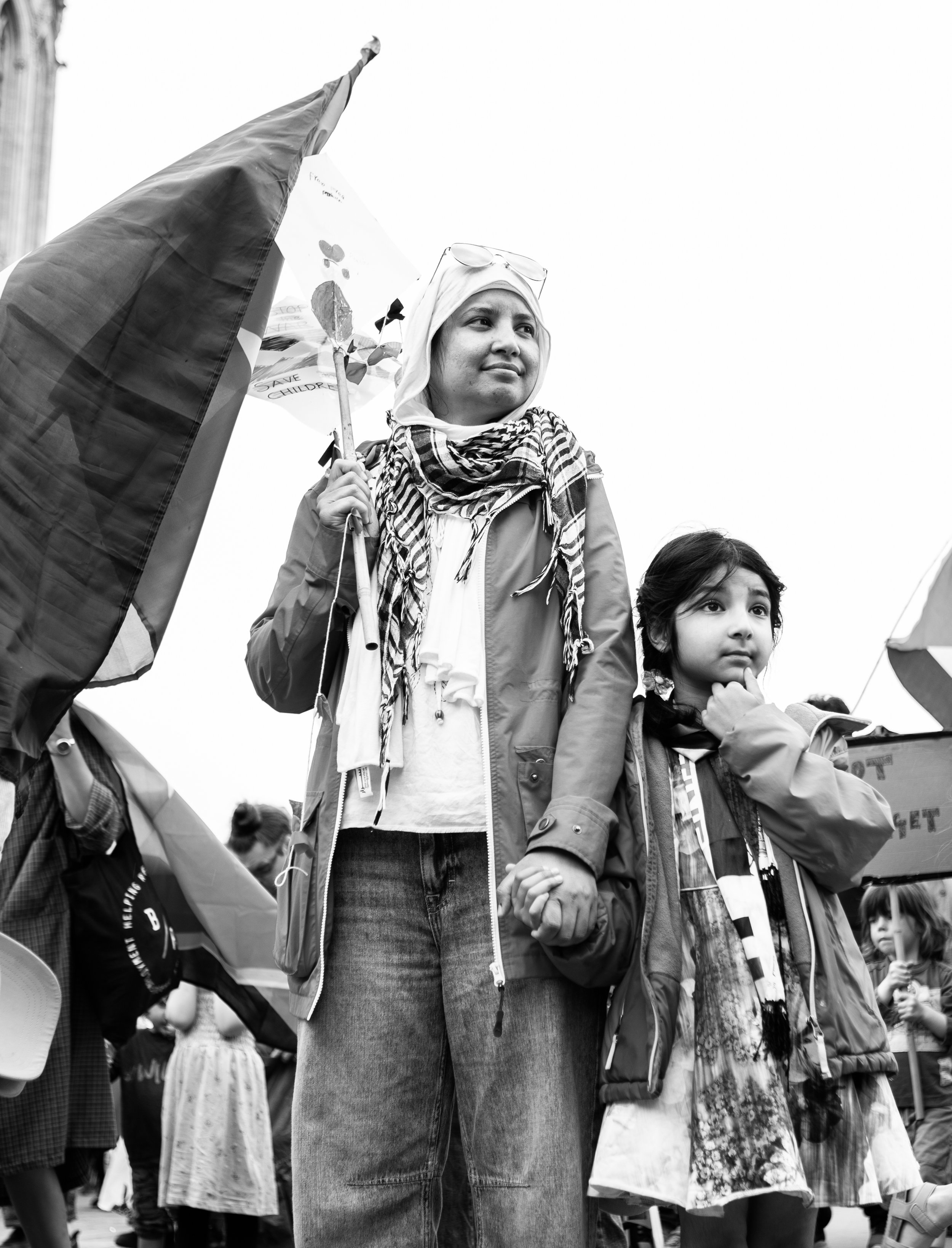 A woman and a young girl holding hands at a protest or rally, standing among a crowd of children.
