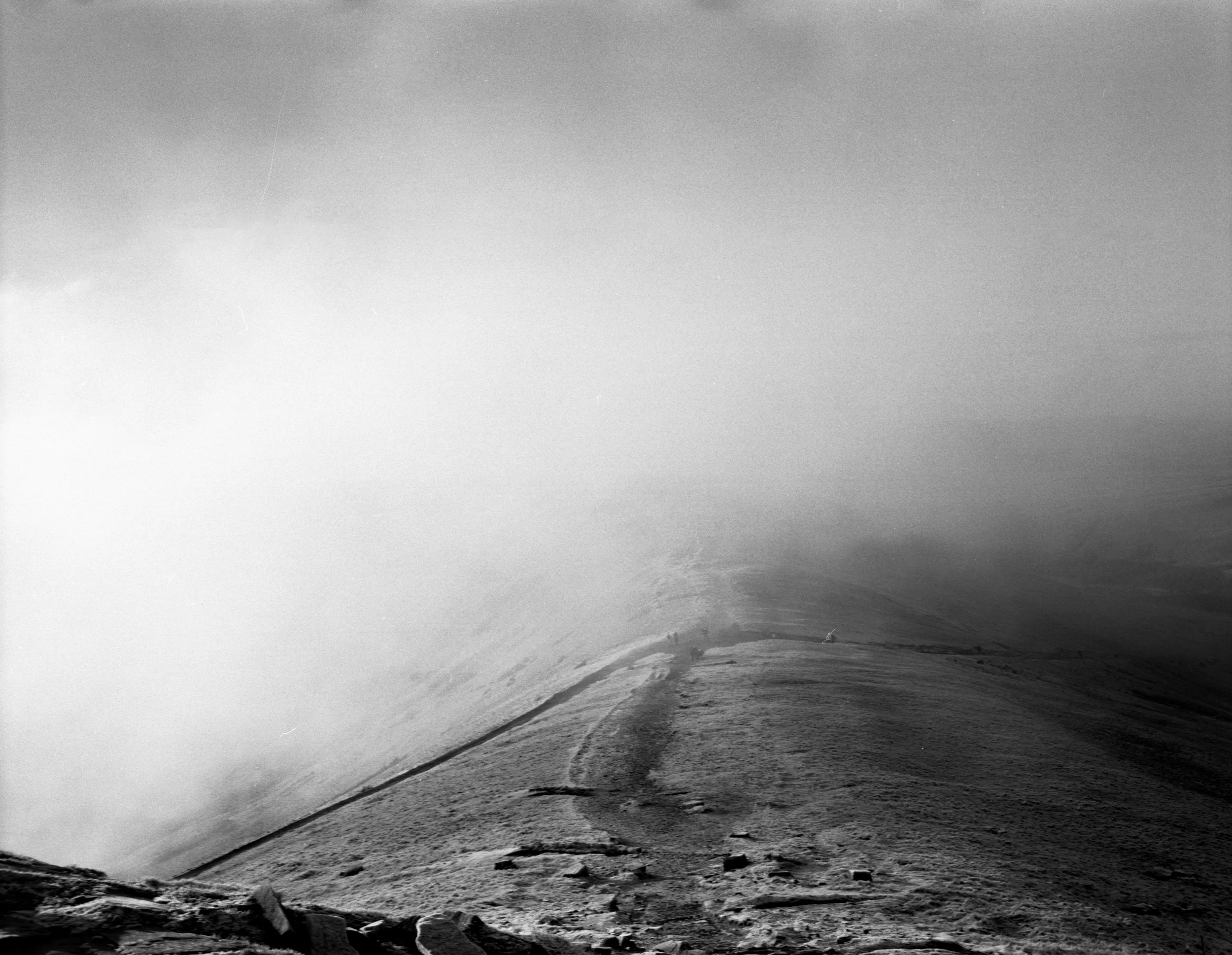 A black and white photo of a windswept desert landscape with rocky terrain and a distant horizon obscured by dust or fog.