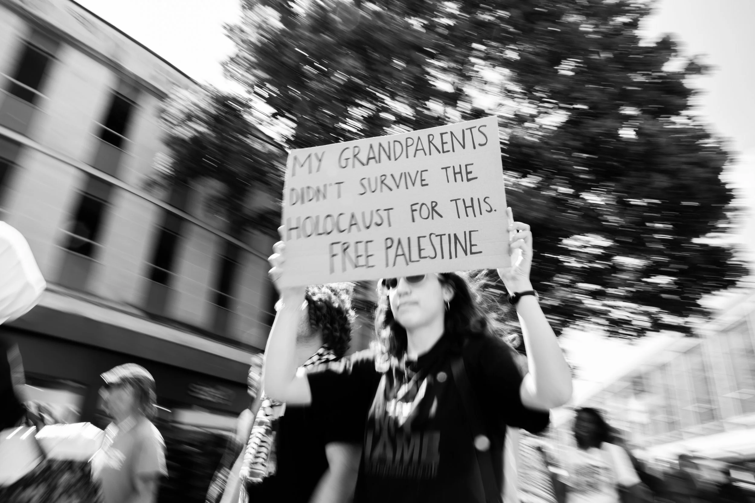 A woman holding a sign that says 'My grandparents didn't survive the Holocaust for this. Free Palestine' during a protest.