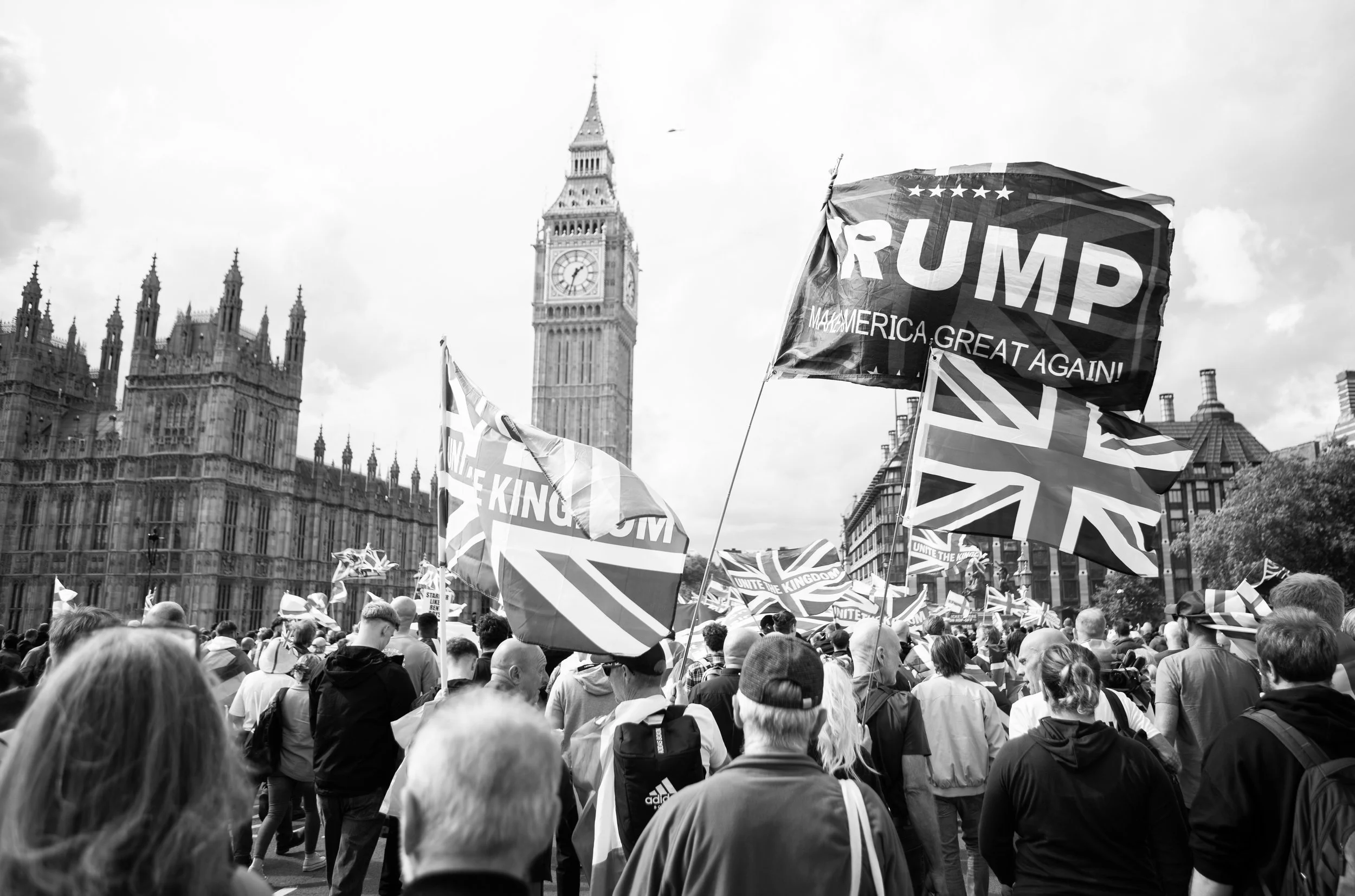 Crowd of protesters holding Union Jack flags and a Trump campaign flag in front of the UK Parliament with Big Ben in the background.
