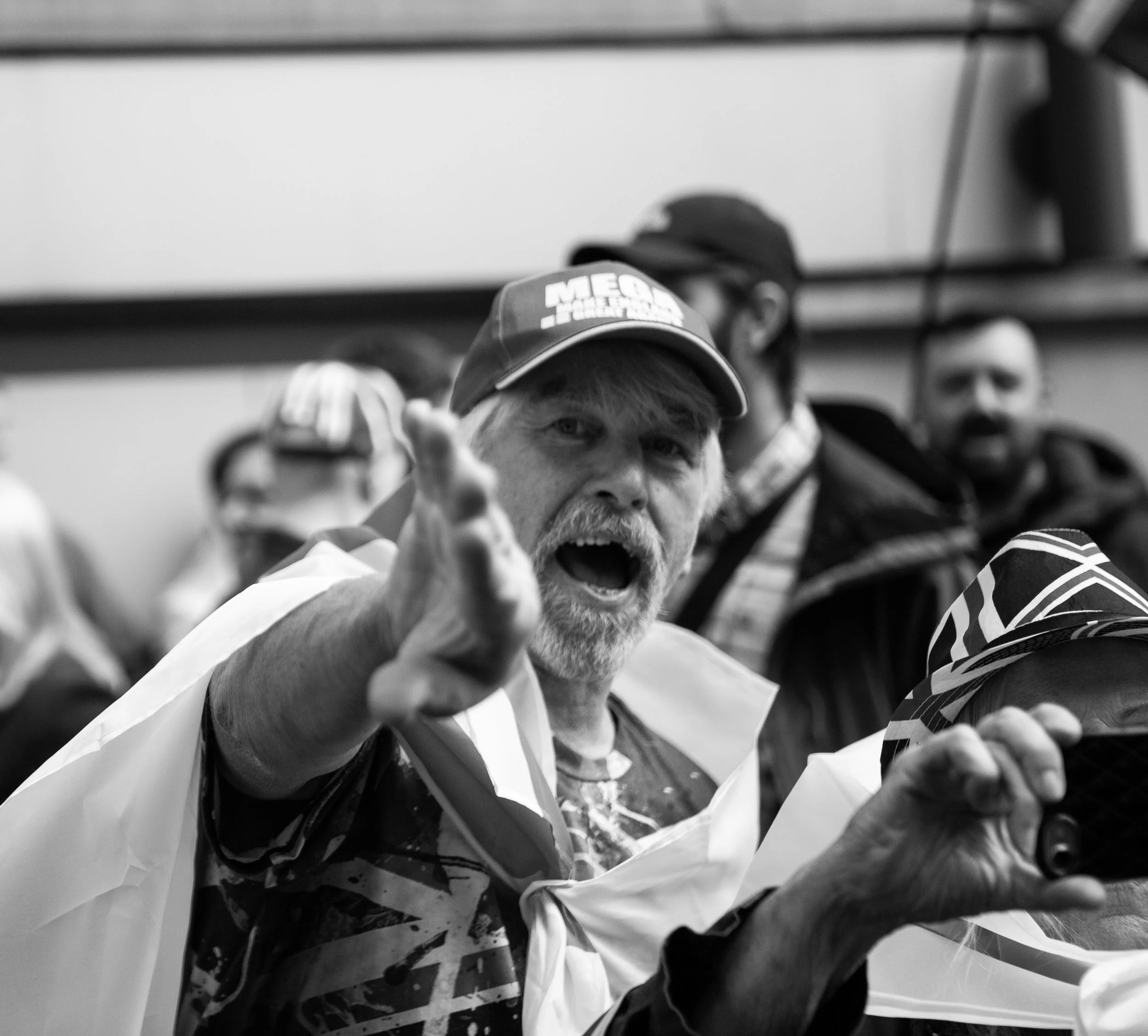 A black-and-white photo of an older man shouting and reaching out with his hand, surrounded by people.