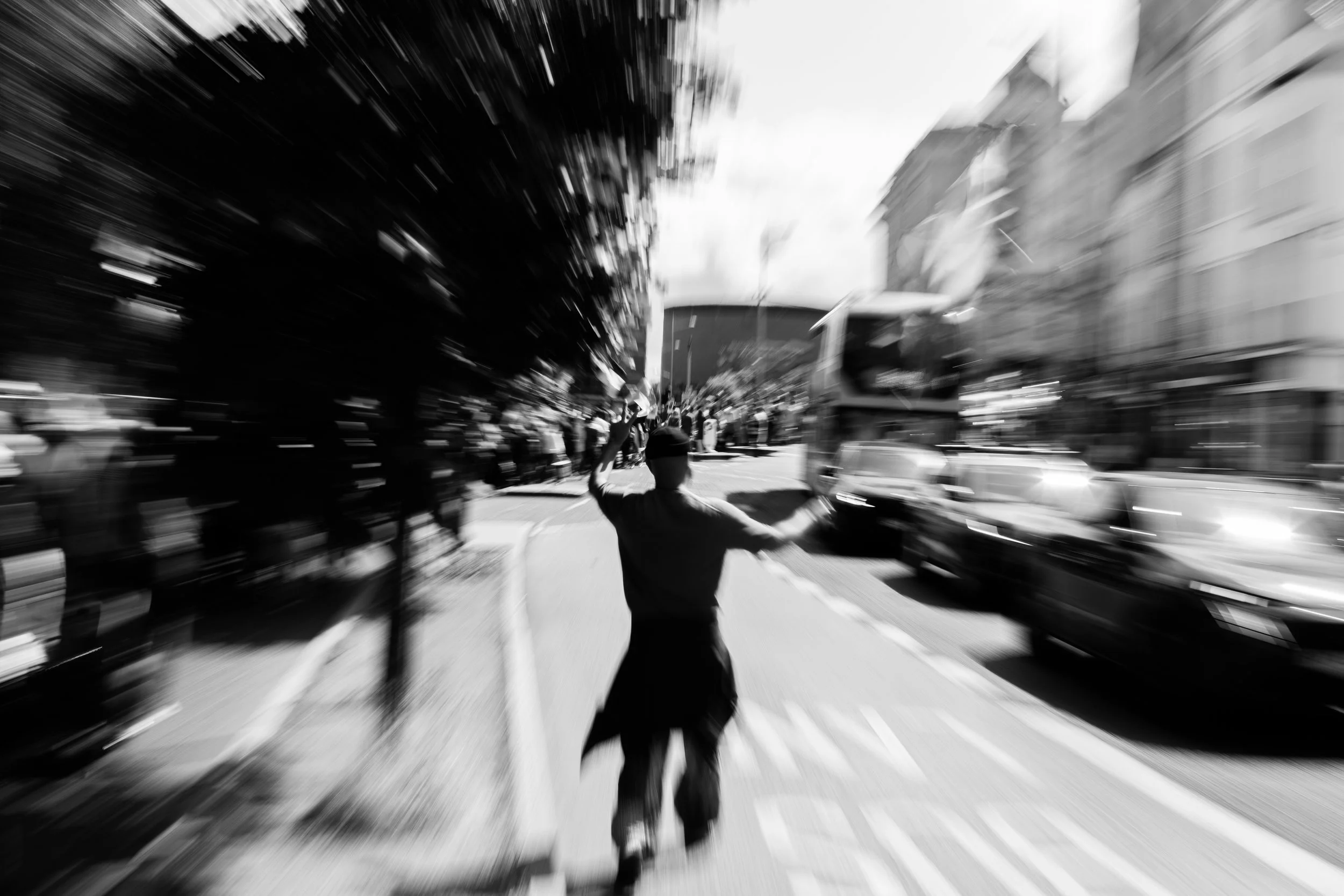 A person standing in the middle of a busy street, raising an arm, with motion blur of cars and buildings around.