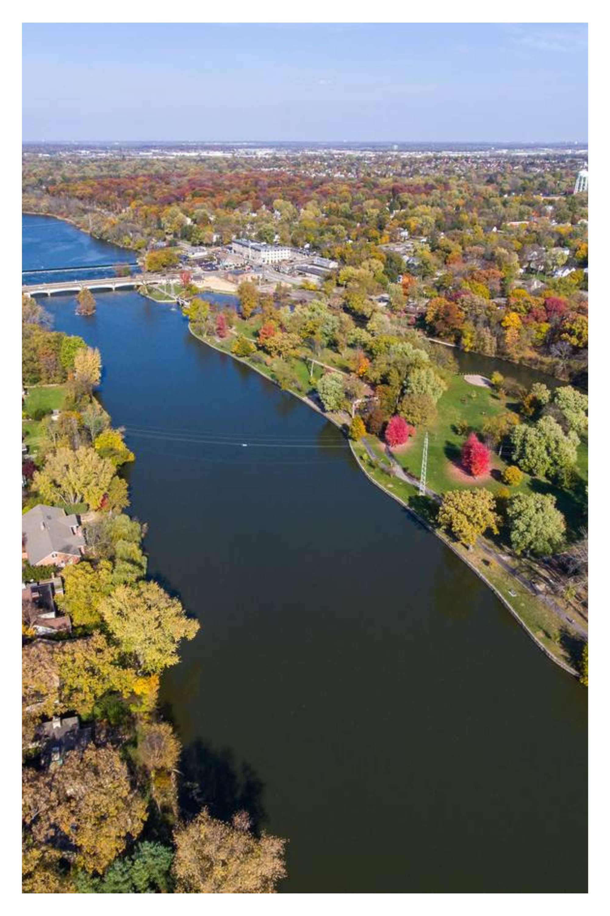 Aerial view of Fox River with a bridge, surrounded by colorful fall trees and a park, with a Geneva, Illinois and neighboring towns in the background.