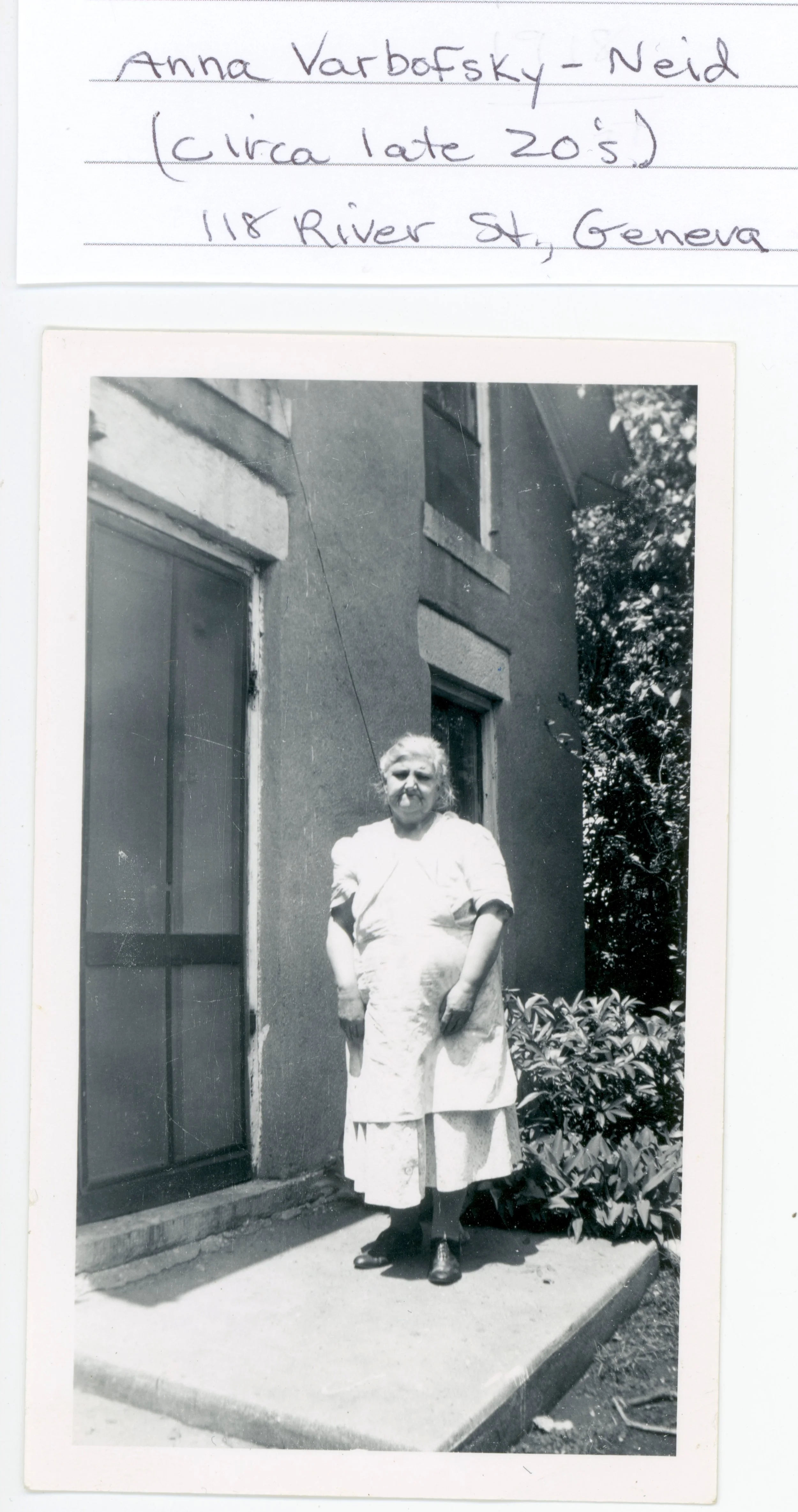 An elderly woman, Anna Varbofsky-Neid, standing before the original front door of the property.