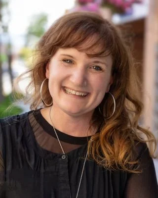 Two minimalist beige ceramic vases, one with dried flowers, placed on a neutral-colored surface against a plain background.