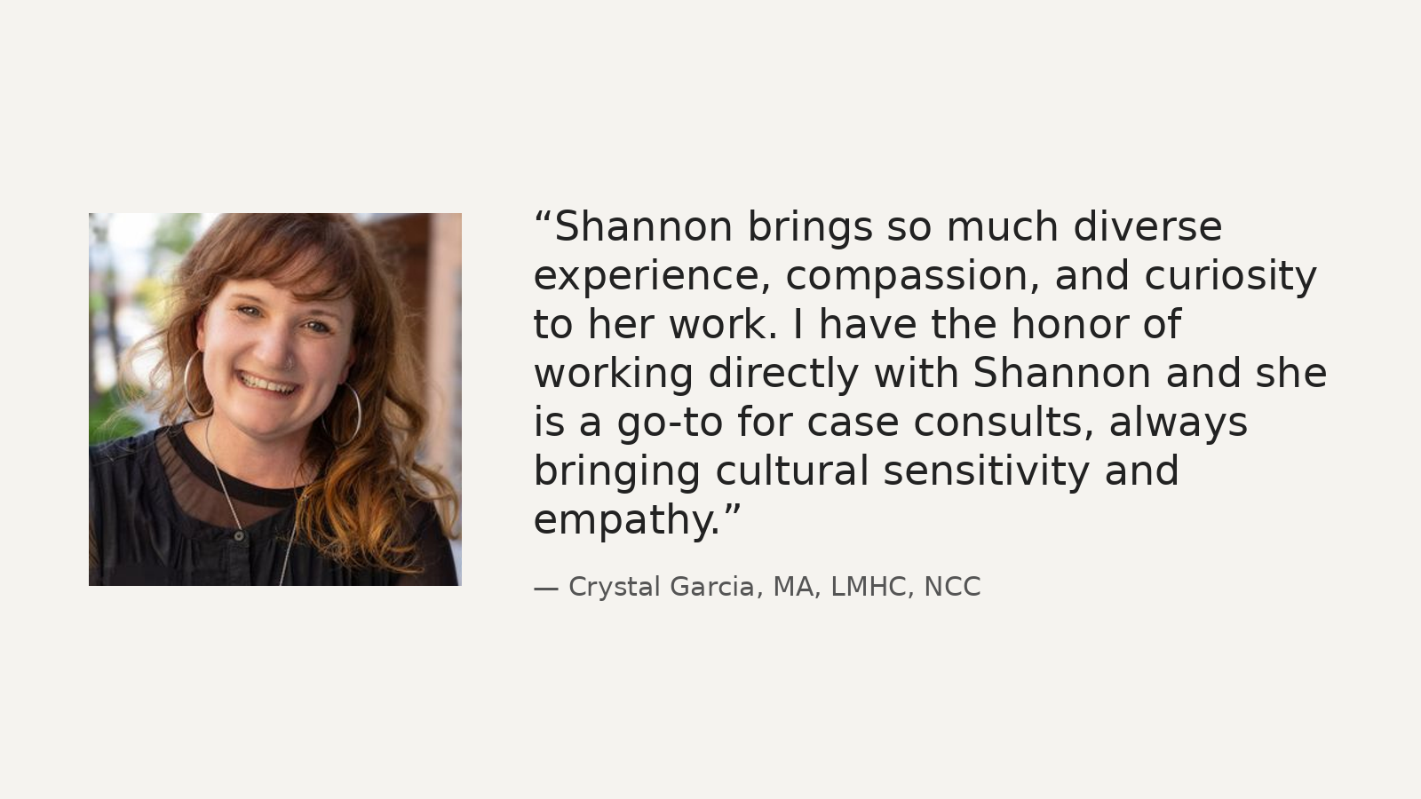A portrait of a woman with shoulder-length red hair, smiling, wearing a black top, earrings, and a necklace, set outdoors.