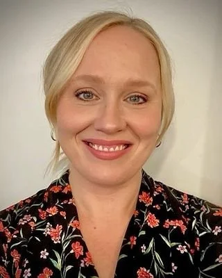 A woman with blonde hair and a floral top smiling for a photo.