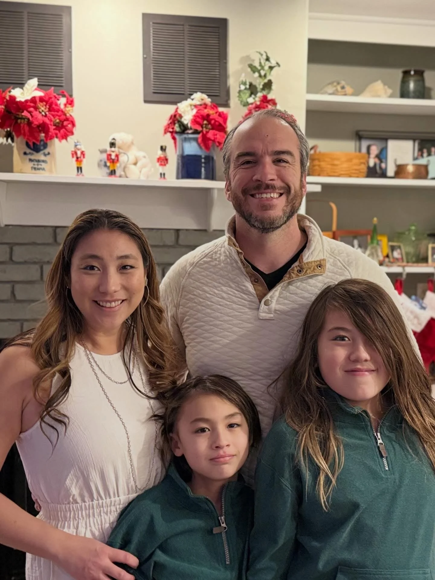 Bradley Merkl-Gump posing with family in front of a fireplace decorated for Christmas, with poinsettias, Nutcracker figures, framed photos, and holiday decorations.