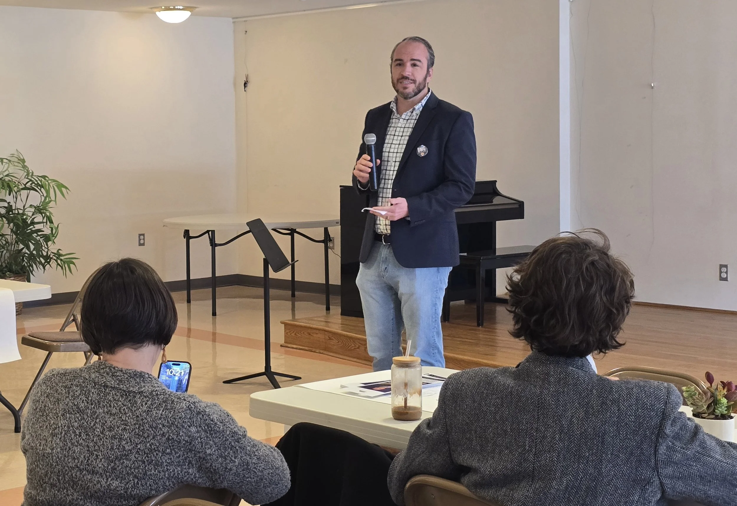 Bradley Merkl-Gump holding a microphone and a notepad speaking to an audience.