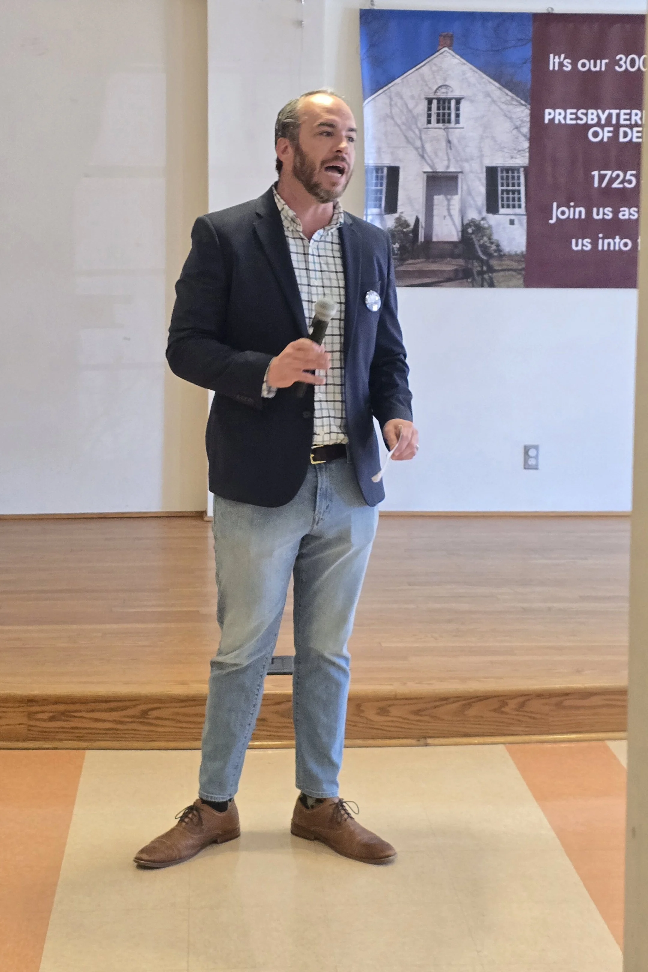 Bradley Merkl-Gump speaking at an indoor event, holding a microphone.