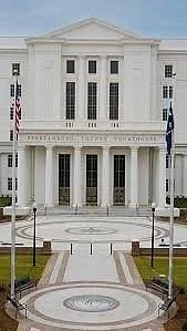 Front view of a large, white, neoclassical-style courthouse building with columns and an American flag.