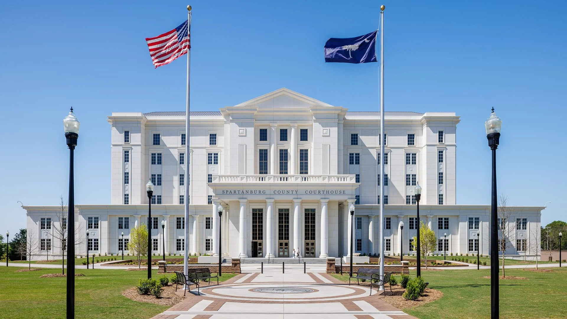 Front view of Spartnburg County Courthouse, a white neoclassical building with columns and flags flying in front, on a sunny day with clear blue sky.