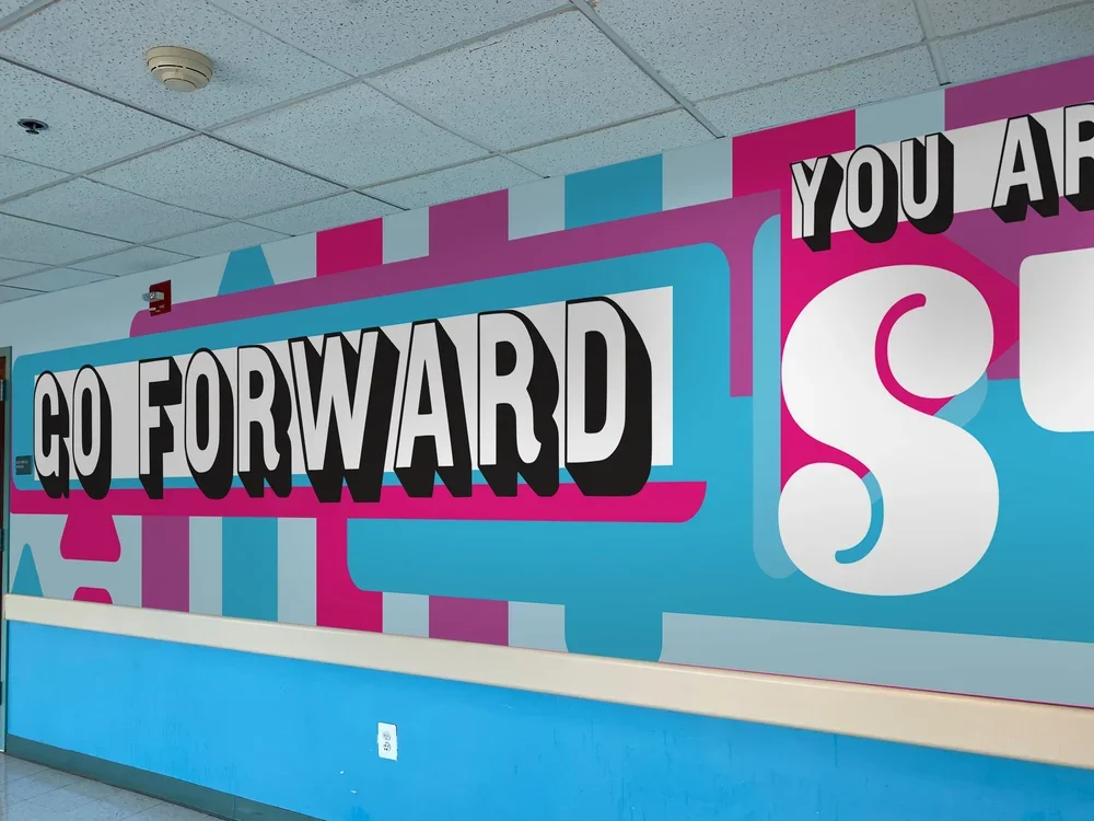 Colorful wall mural with the phrase "Go Forward" in large black and white letters on a pink background, with additional text partially visible.