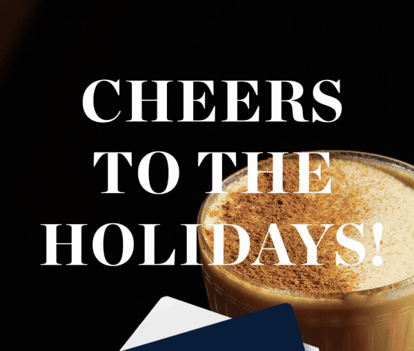 A festive holiday greeting card with the message "Cheers to the Holidays!" written in white text. Part of a coffee or cocktail drink with foam and cinnamon is visible on the right side, and a white napkin with a dark blue edge is partly visible at the bottom.