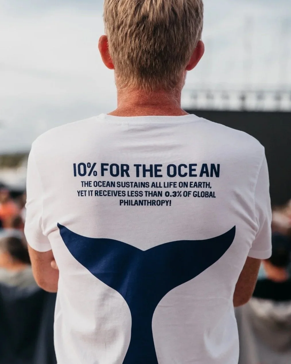 Back of a person wearing a white T-shirt with a whale tail graphic and text promoting ocean conservation.
