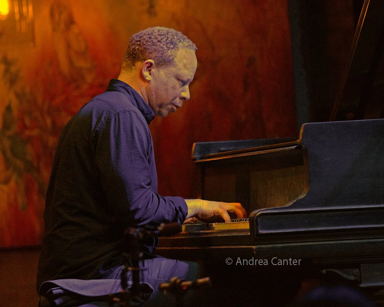 Man playing the piano in a dimly lit room with a warm color background.