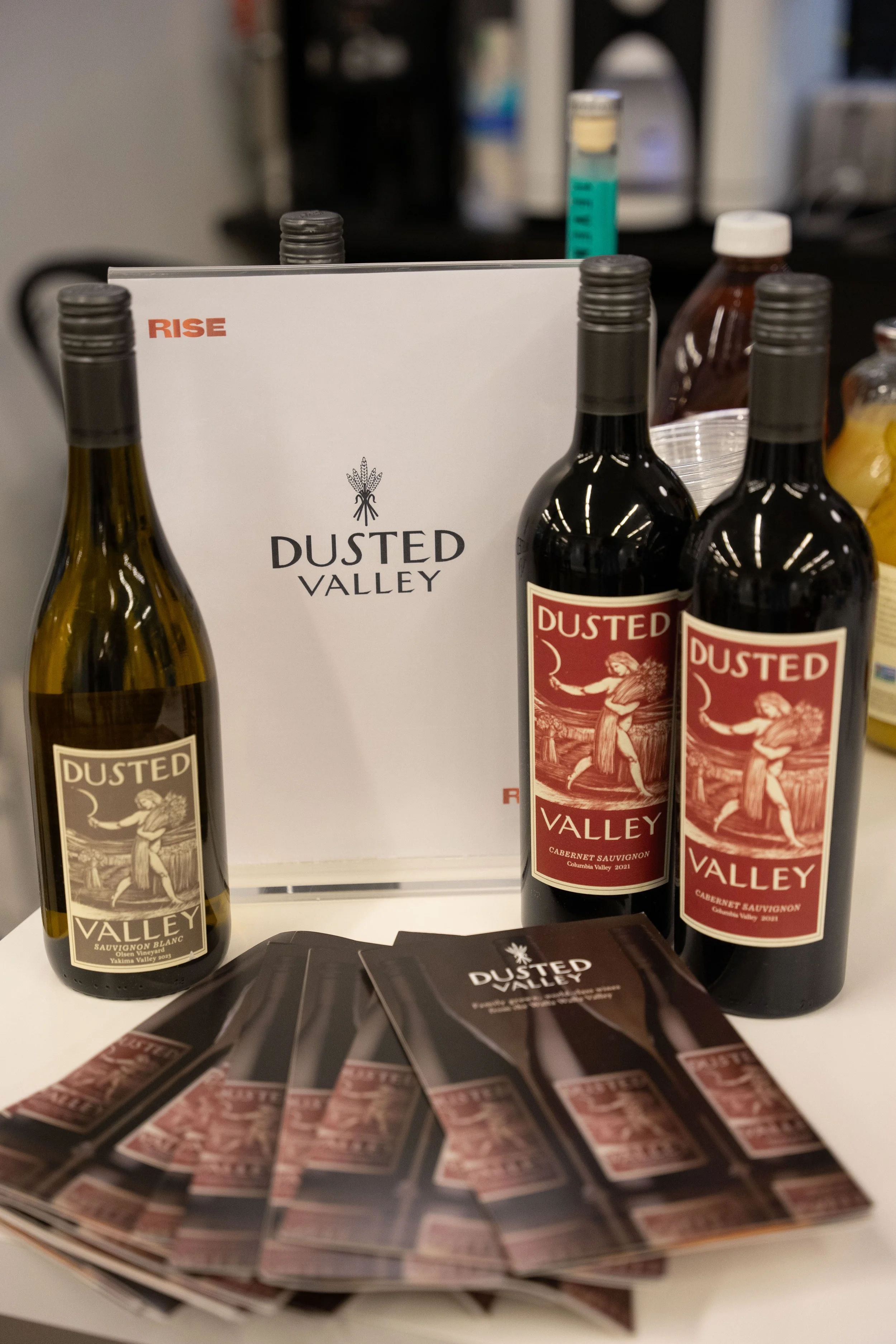 Display of Dusted Valley wine bottles, including Sauvignon Blanc and Cabernet Sauvignon, with brochures or flyers promoting the winery.