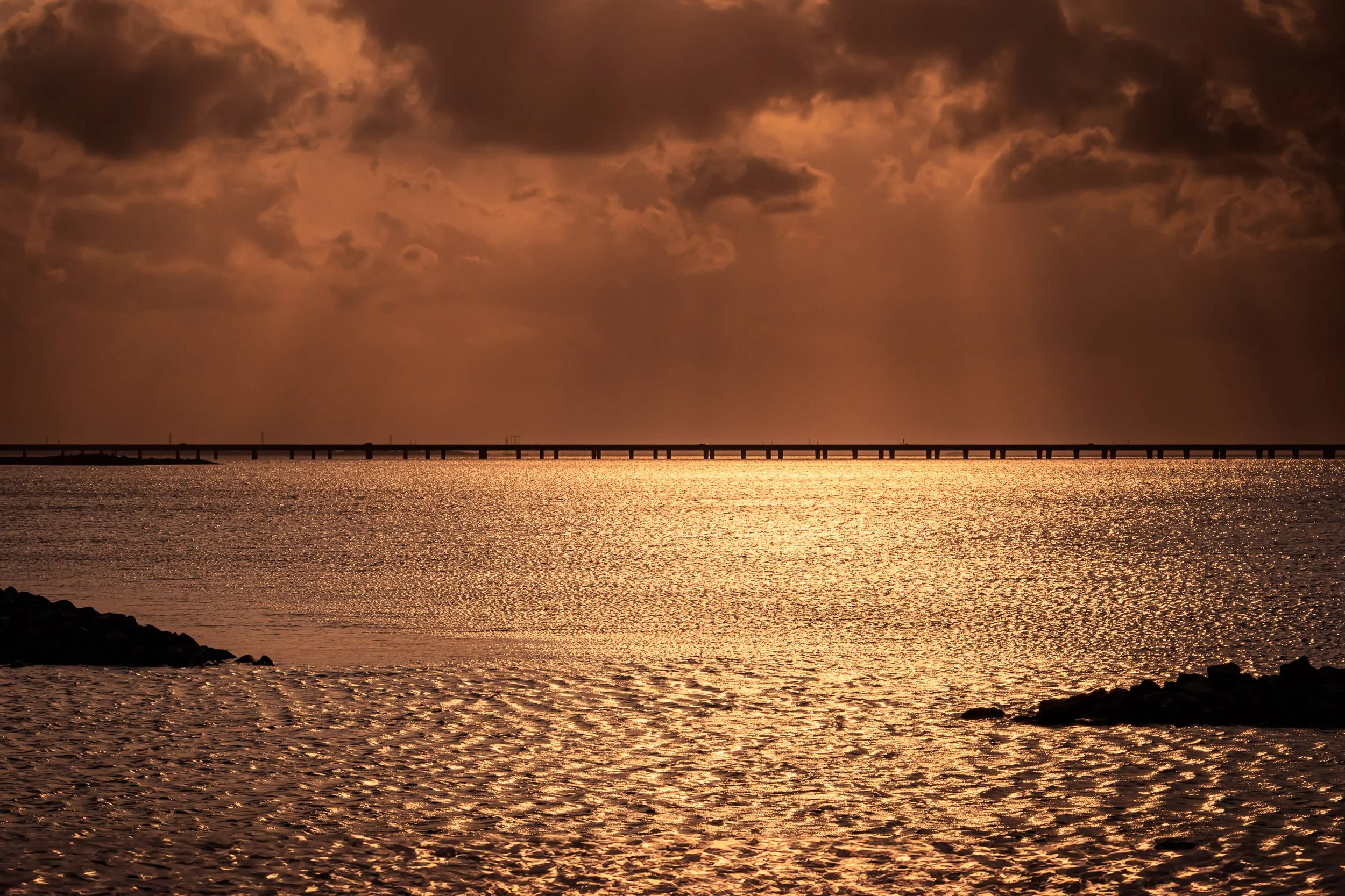 Burnished Divide

Golden sunlight breaking through clouds over Lake Pontchartrain in Bucktown, New Orleans, reflecting across rippled water with the Causeway bridge silhouetted on the horizon.
