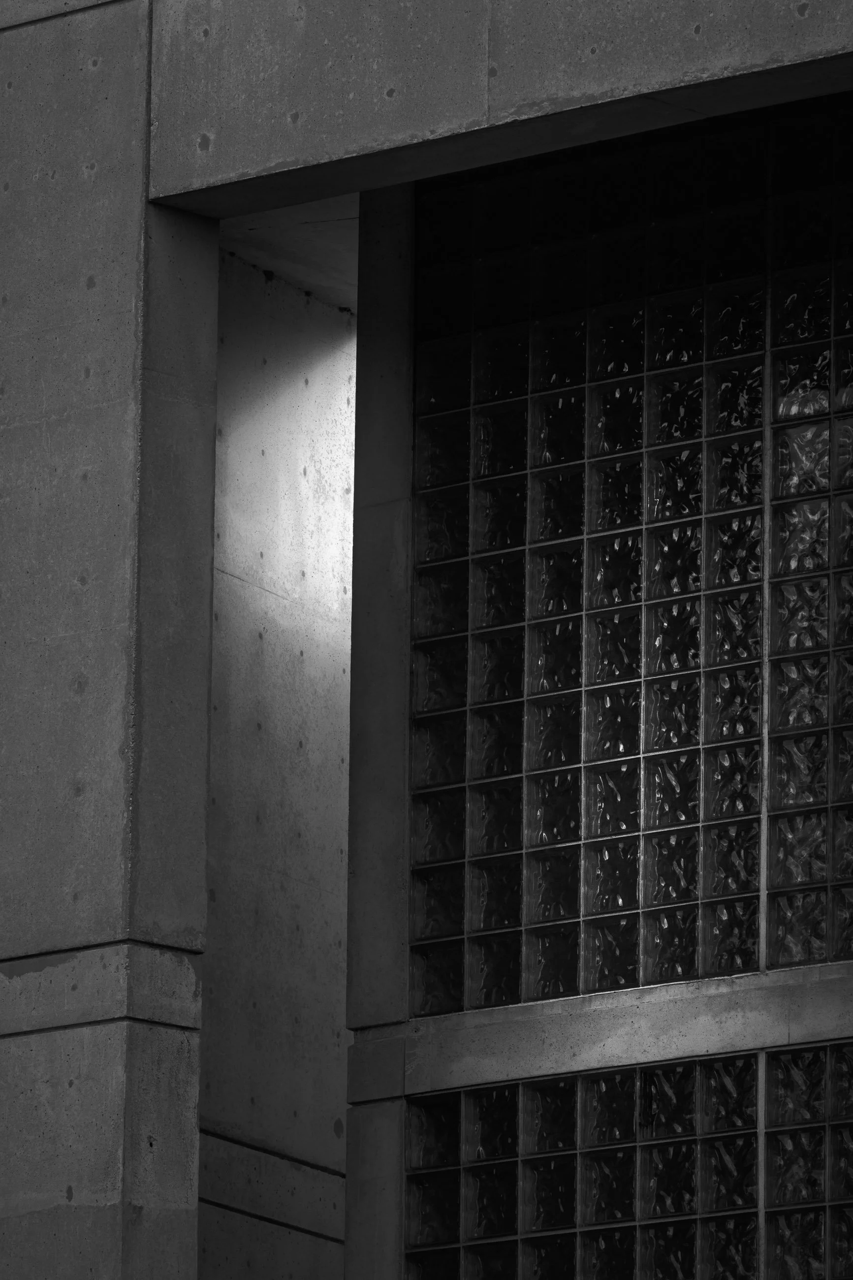 Filtered Luminance

Black-and-white photograph of a modern concrete building with a recessed opening beside a glass block wall. Indirect light enters through the narrow airspace between the structures.