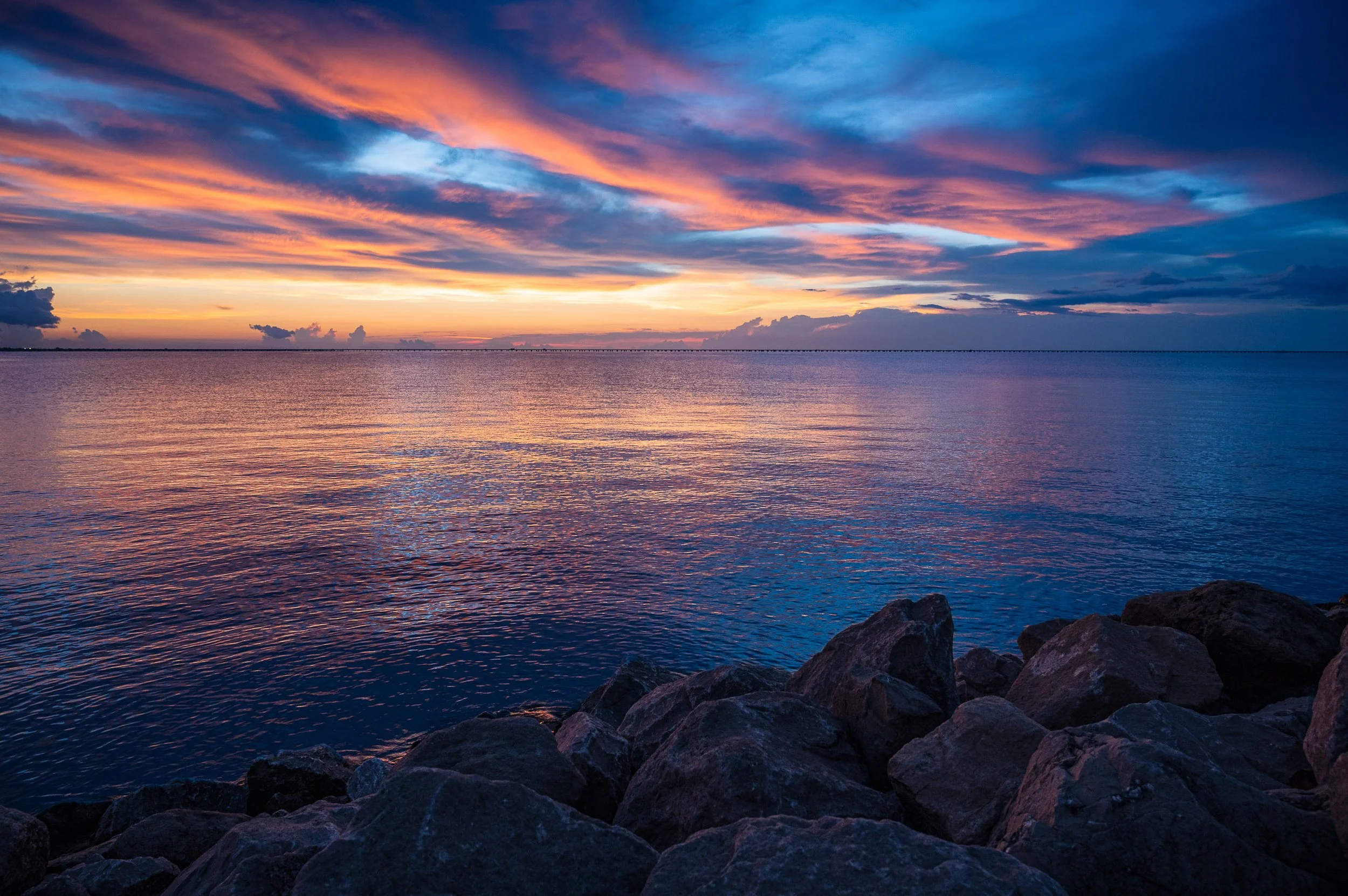 Afterlight

Vibrant pink and blue after-sunset glow over Lake Pontchartrain at West End in New Orleans, reflected across calm water with rocky shoreline in the foreground.