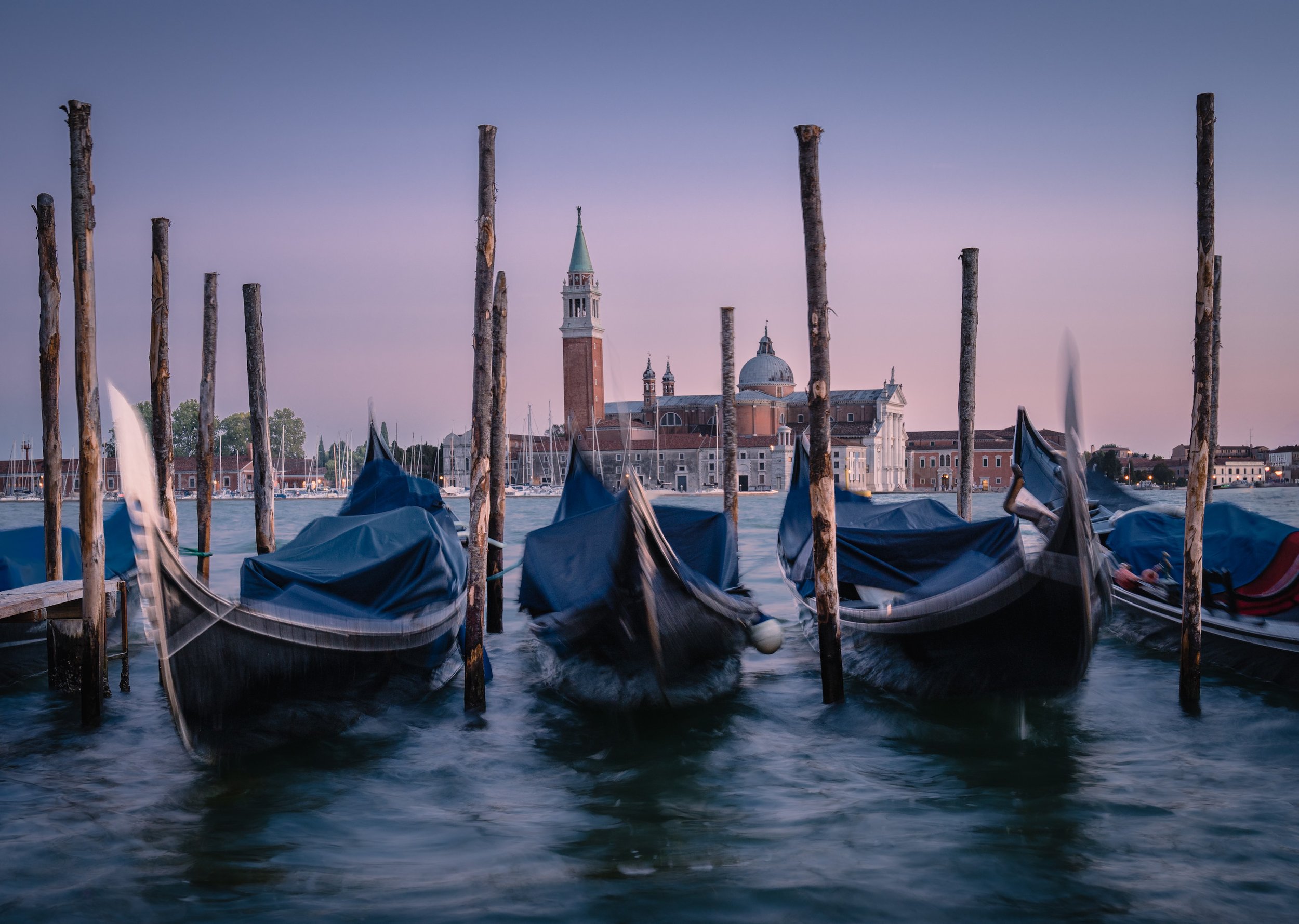 Of Moments and Ages

Motion-blurred gondolas and wooden mooring posts on the water at blue hour, with San Giorgio Maggiore across the lagoon in Venice.