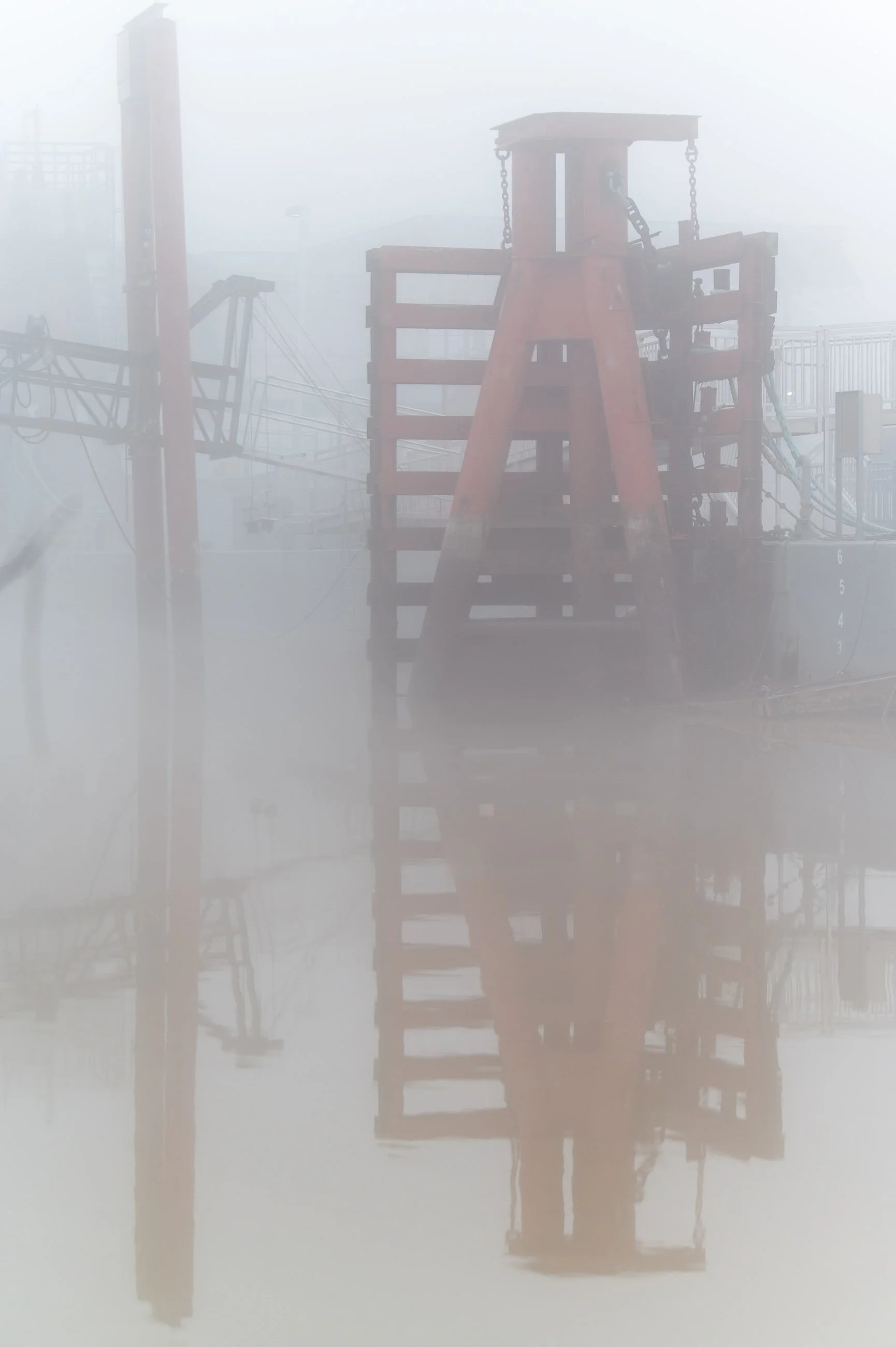 Emergent Symmetry

A reddish steel mooring structure stands in dense fog along the Mississippi River, its reflection in the still water creating strong vertical symmetry.