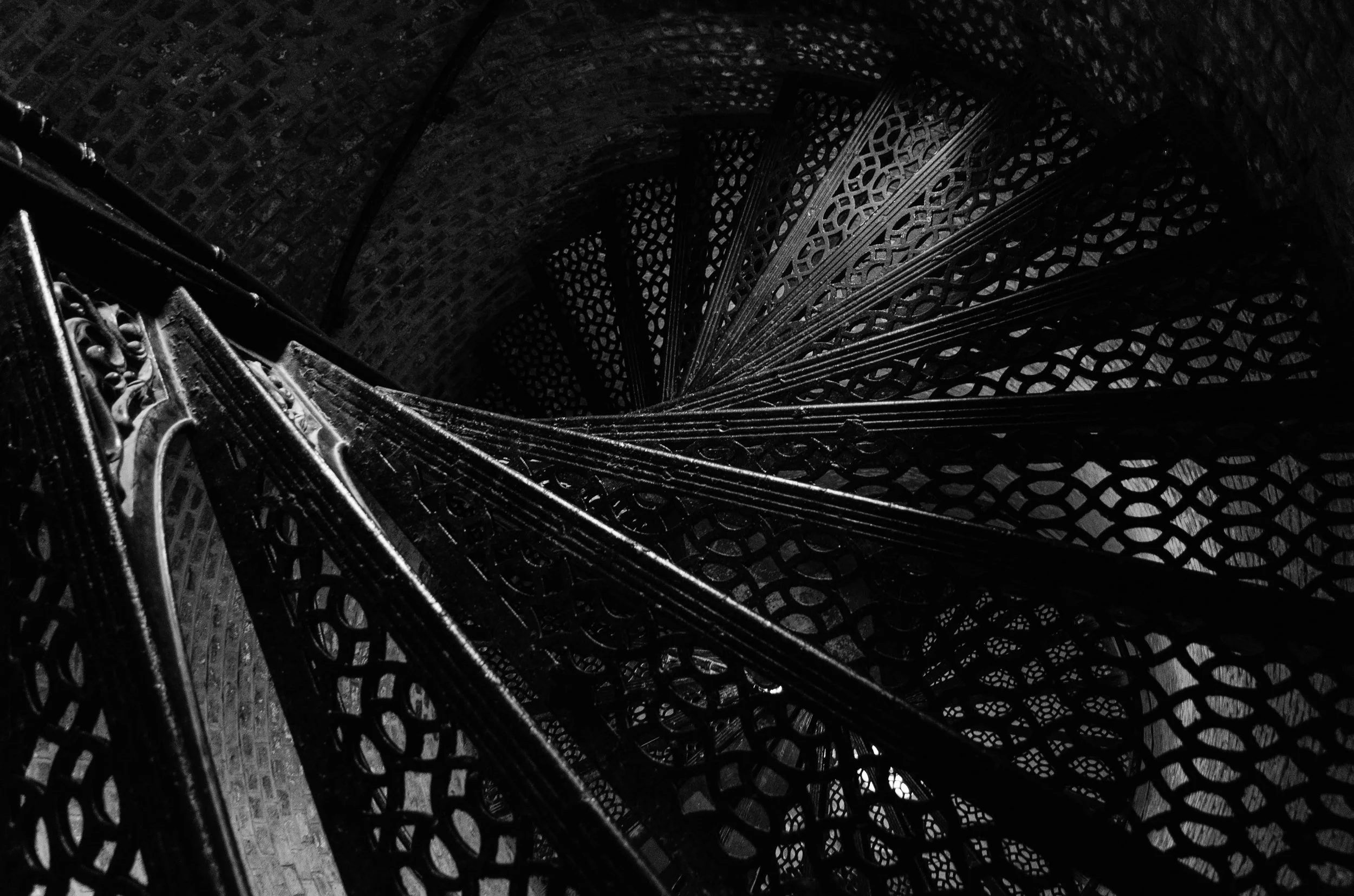 Lattice and Spiral

Black-and-white photograph looking straight down through the wrought-iron spiral staircase inside the Pensacola Lighthouse. Light from below filters upward through the latticework steps.