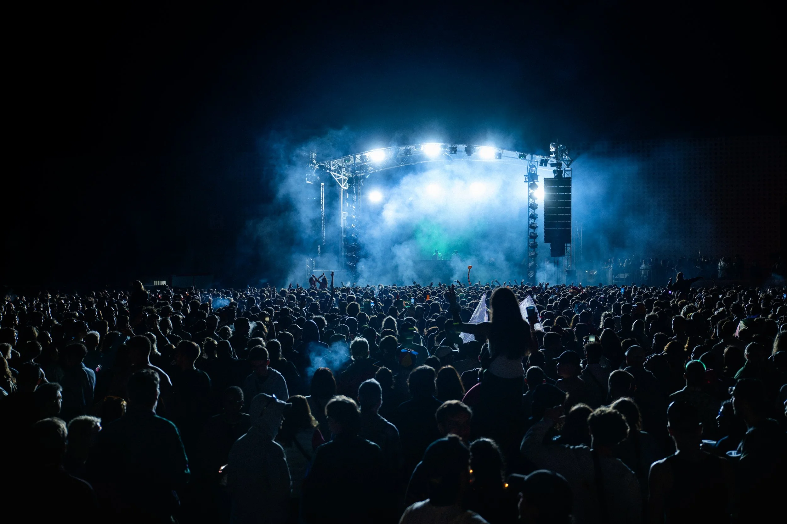 Grand concert en plein air avec un grand public, scène éclairée avec lumières et fumée, ambiance nocturne.