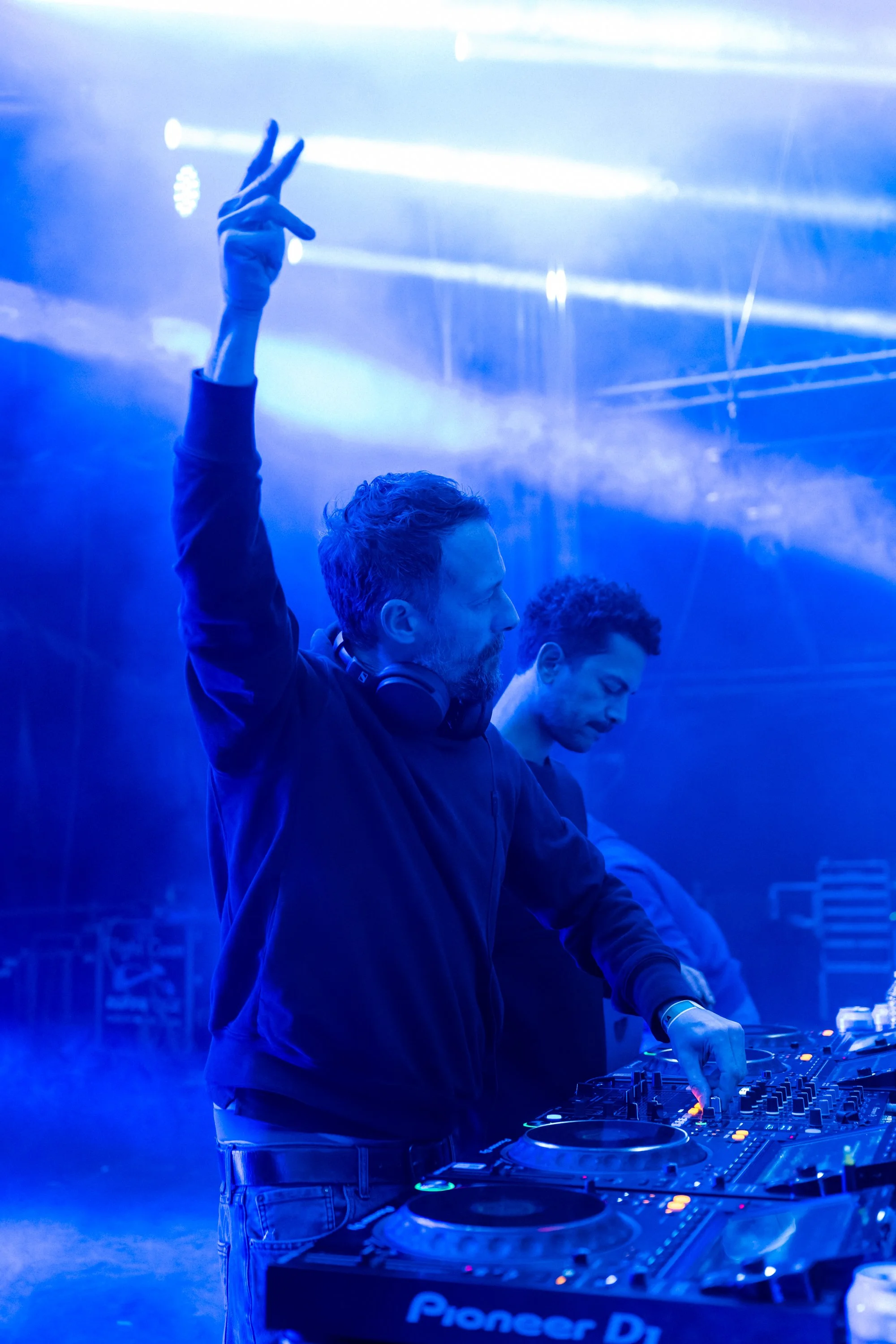 Deux DJ en train de mixer dans une boîte de nuit, avec des lumières bleues et des effets lumineux en arrière-plan.