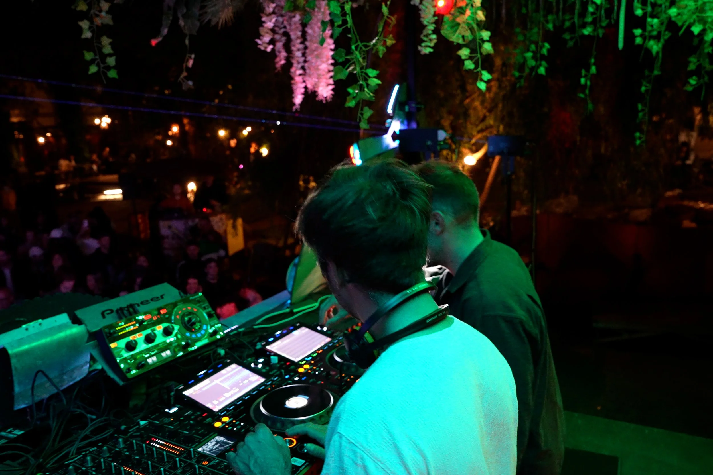 DJ en train de mixer lors d'une soirée en plein air, avec un public en arrière-plan et des lumières colorées dans une ambiance nocturne.